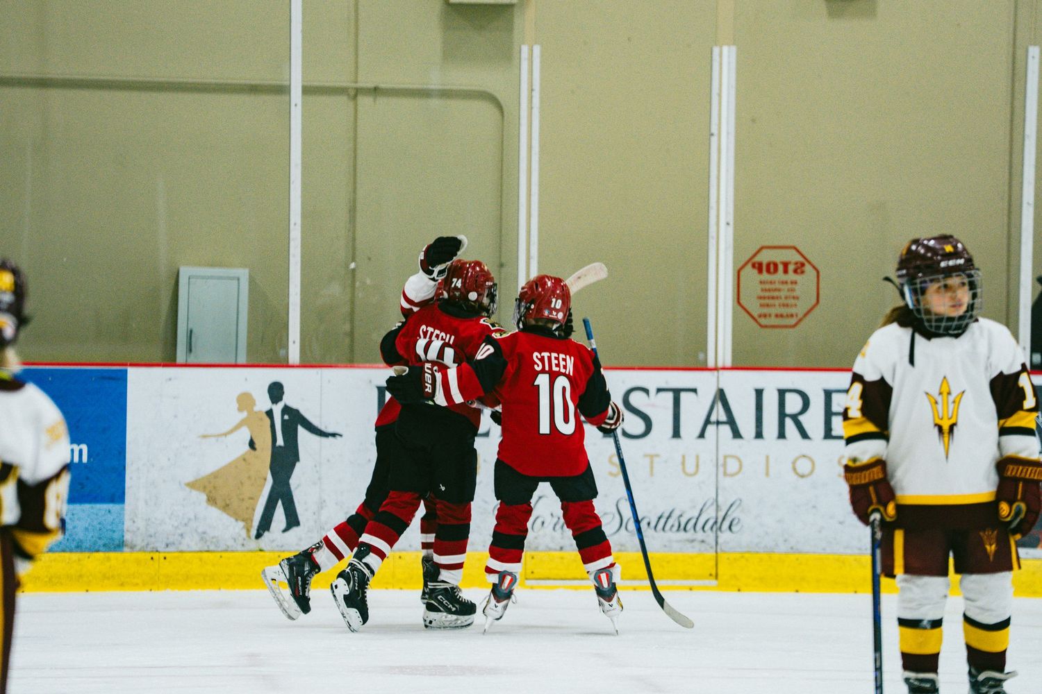 Youth hockey players compete on an indoor ice rink with red and white jerseys during a game.