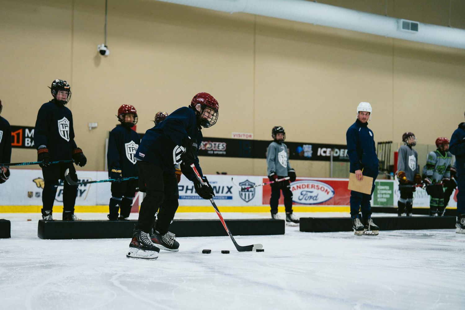 Young hockey players practice puck handling drills on indoor ice rink during youth hockey training camp session.