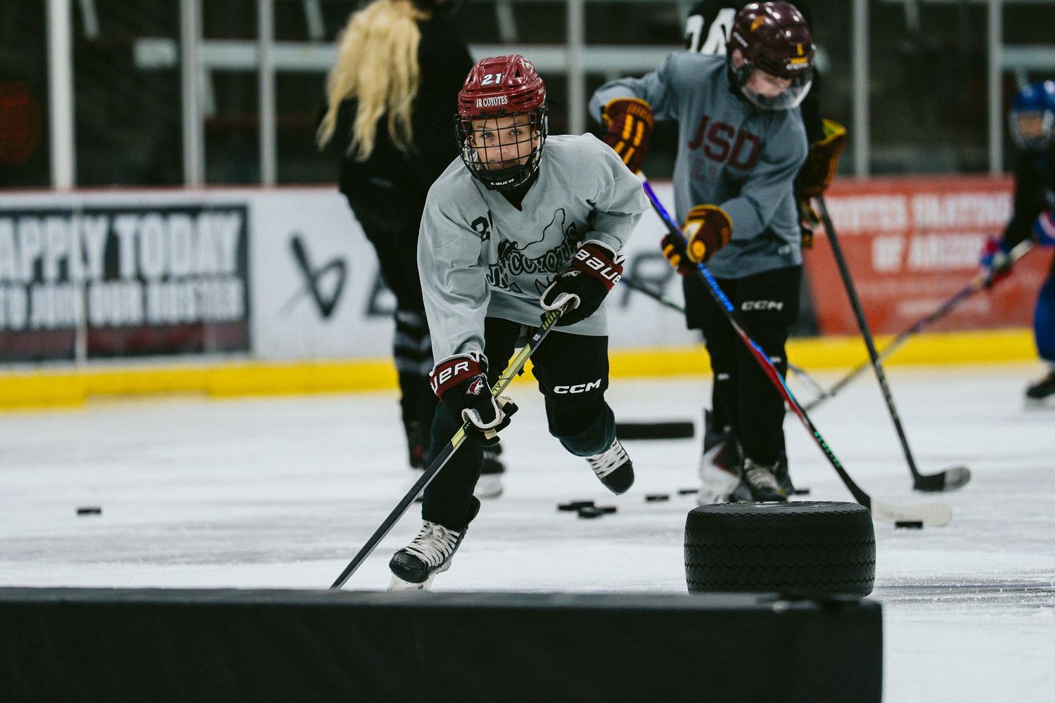 Young hockey player skating with a puck during a youth ice hockey practice drill on an indoor rink.