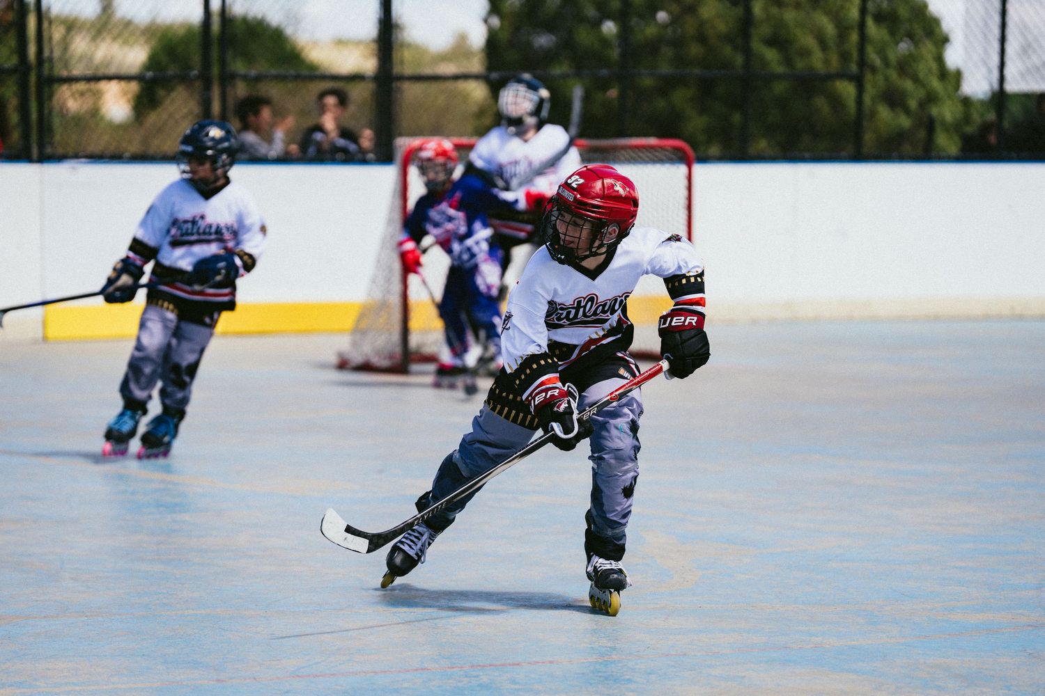 Young roller hockey player in red helmet skating with stick during an outdoor rink game.