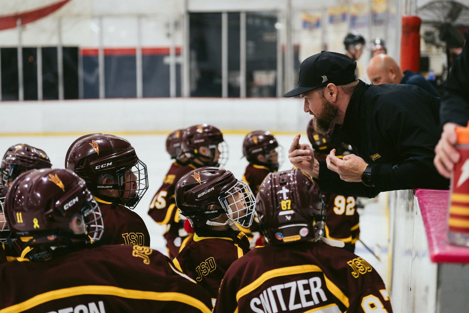 Arizona State Sun Devils hockey coach giving instructions to players on the bench during a game.