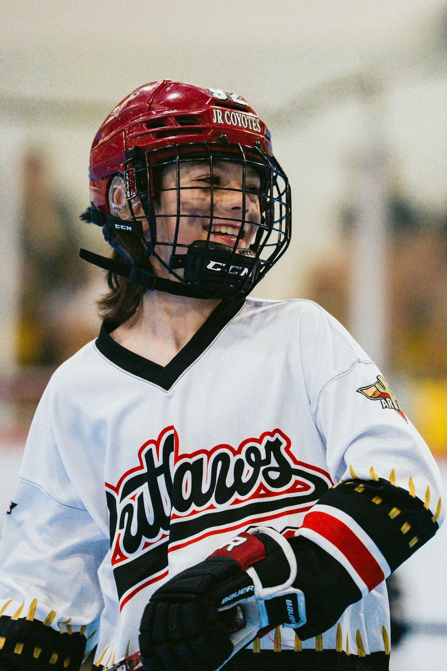 Smiling youth hockey player wearing a red Jr. Coyotes helmet and Outlaws jersey.