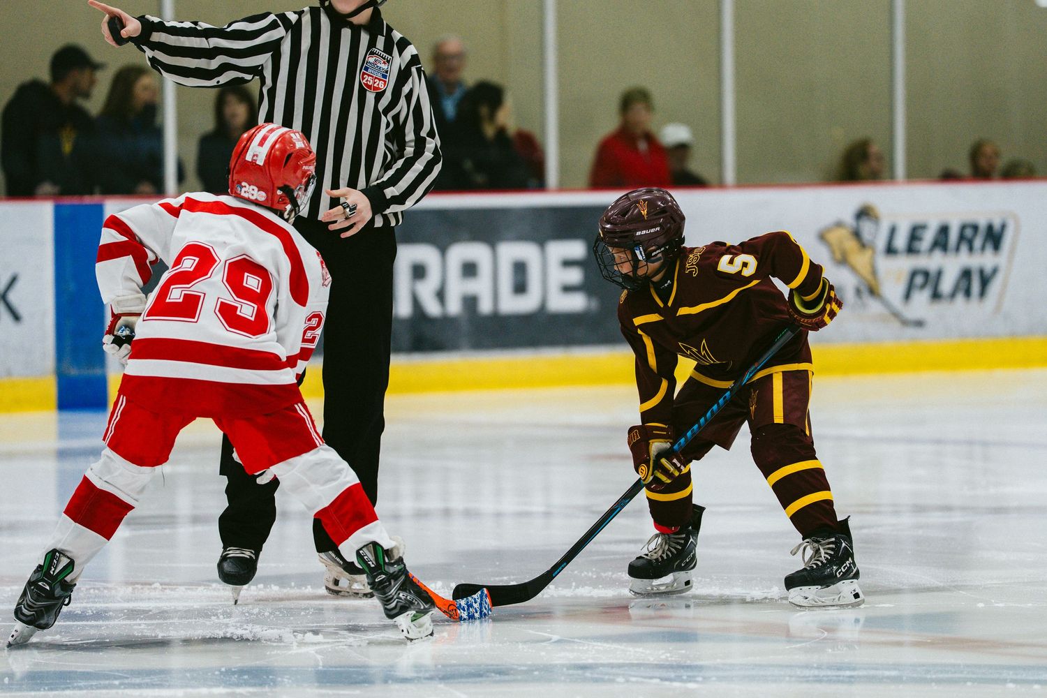 Hockey players in black and red jerseys battle for the puck during an intense game moment.