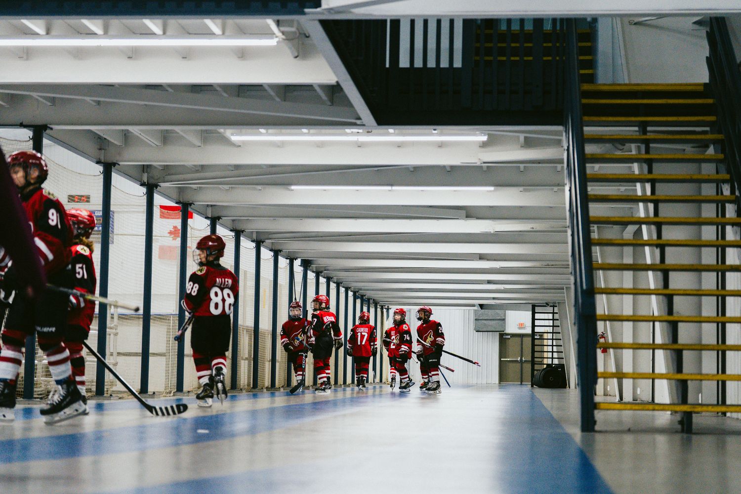 Young hockey players practicing drills on an indoor ice rink with red jerseys.