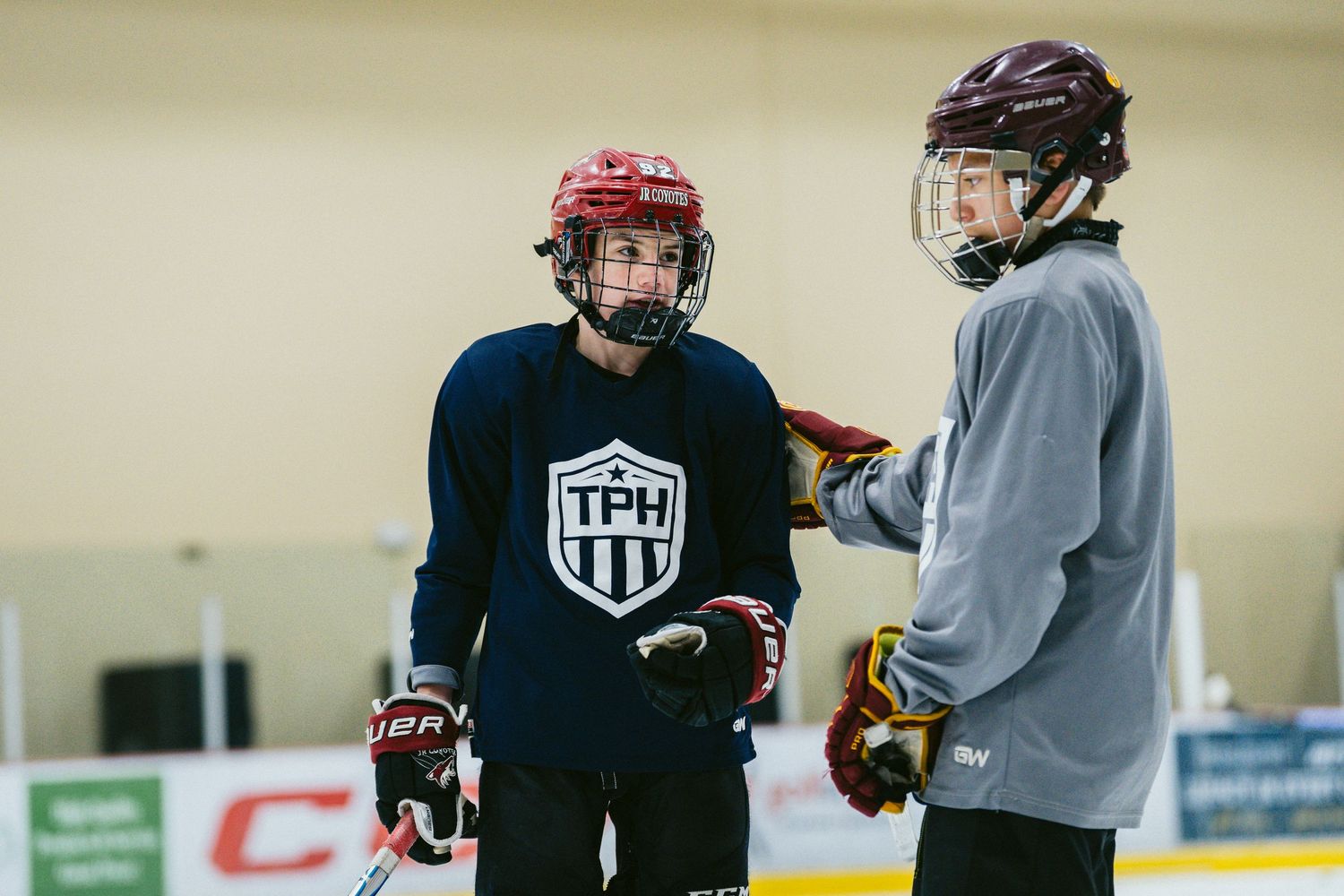 Two young hockey players in helmets talk during TPH ice hockey training practice.