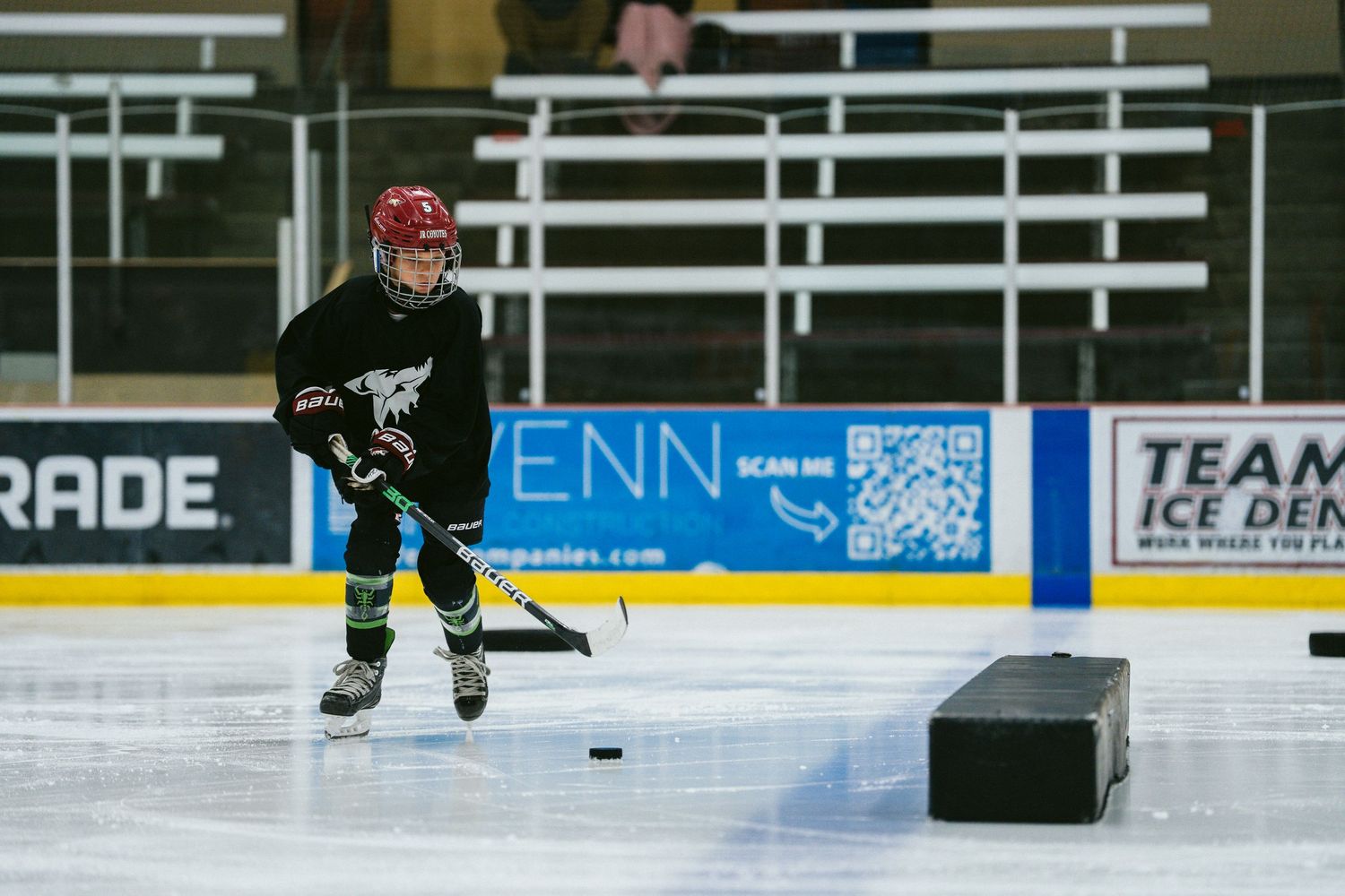 Young hockey player in black jersey practices puck handling drills on indoor ice rink during training session.
