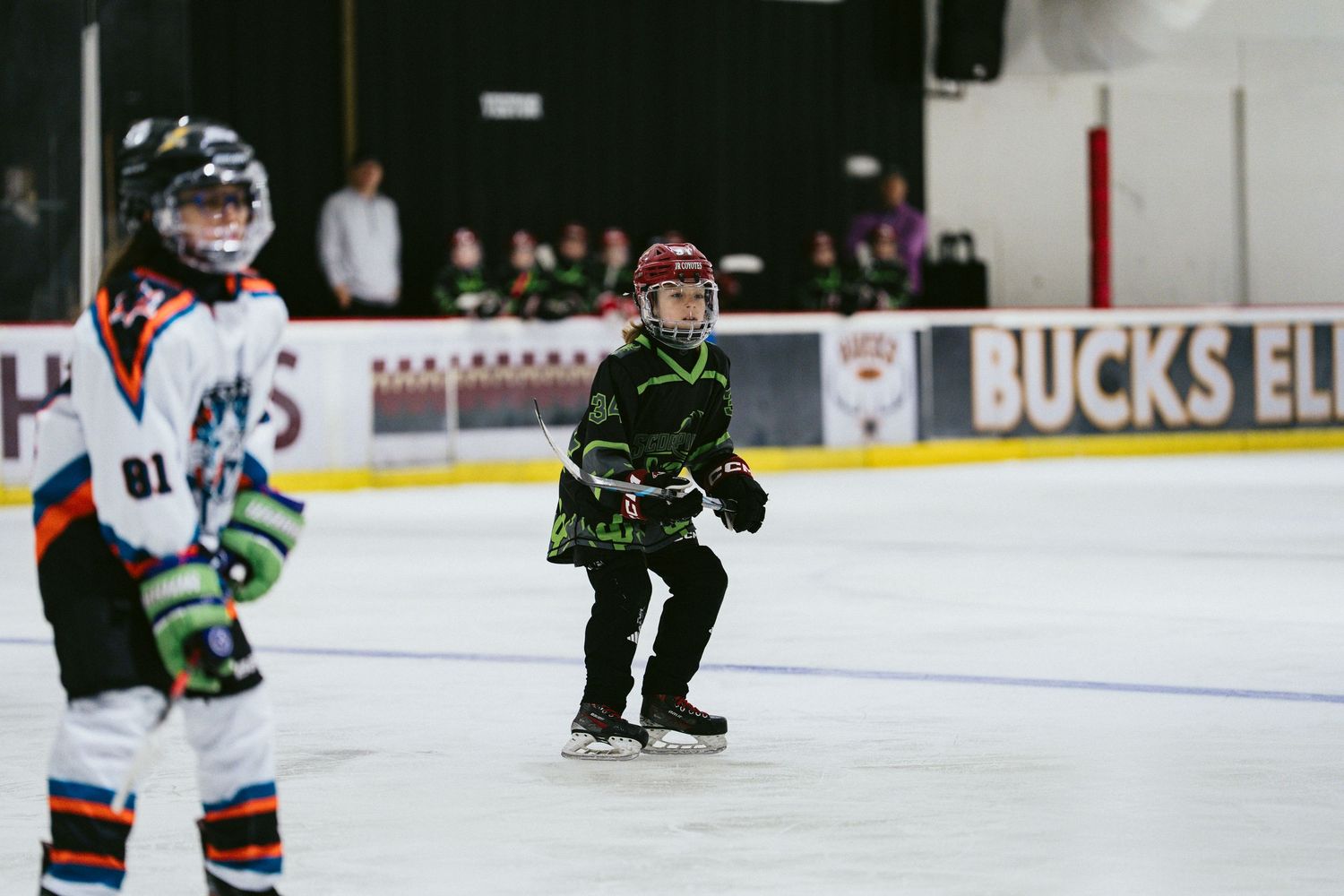 Young hockey player in green jersey skating on indoor ice rink during youth hockey practice session.