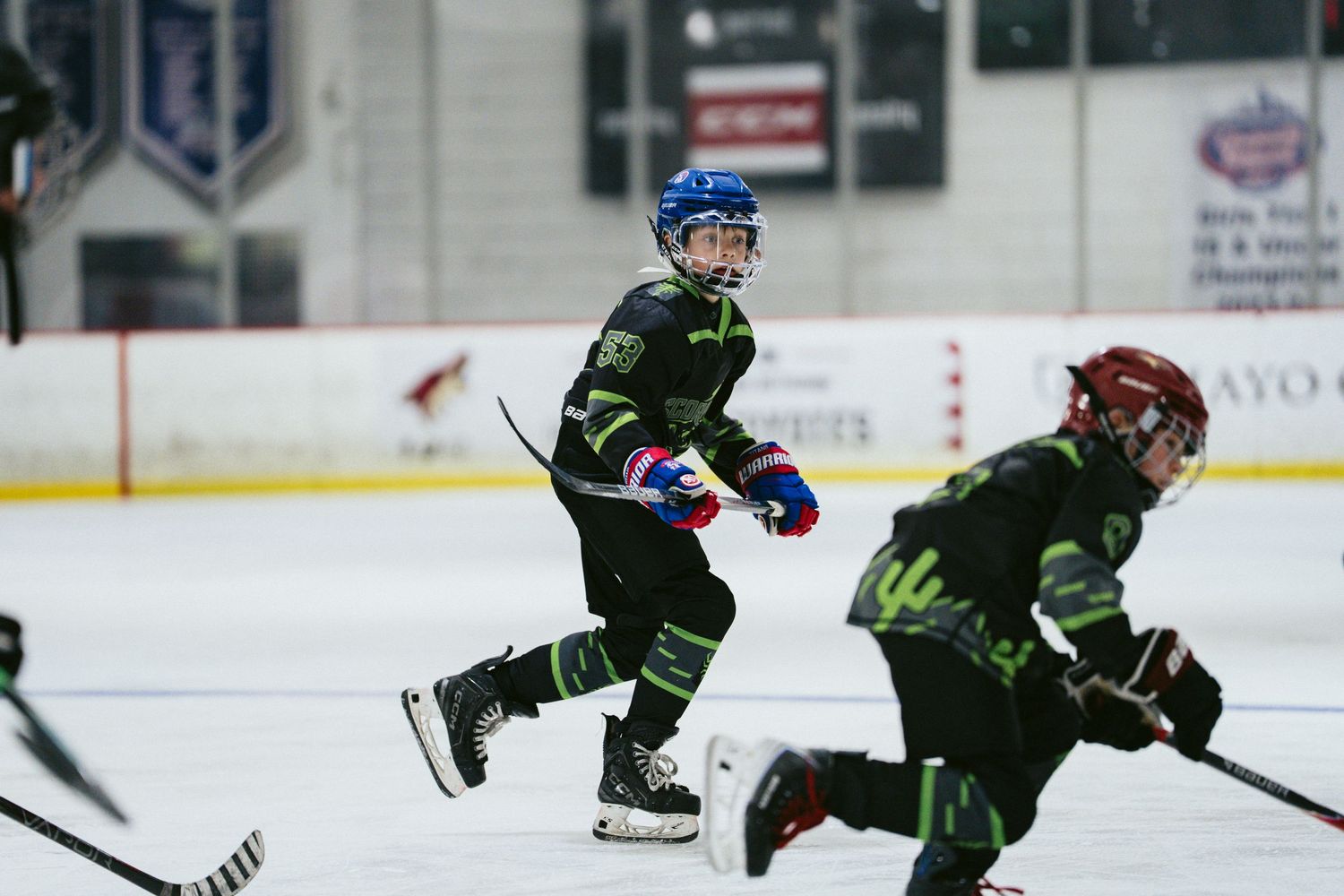 Energetic young hockey player in black green uniform sprints across ice during competitive youth hockey game.