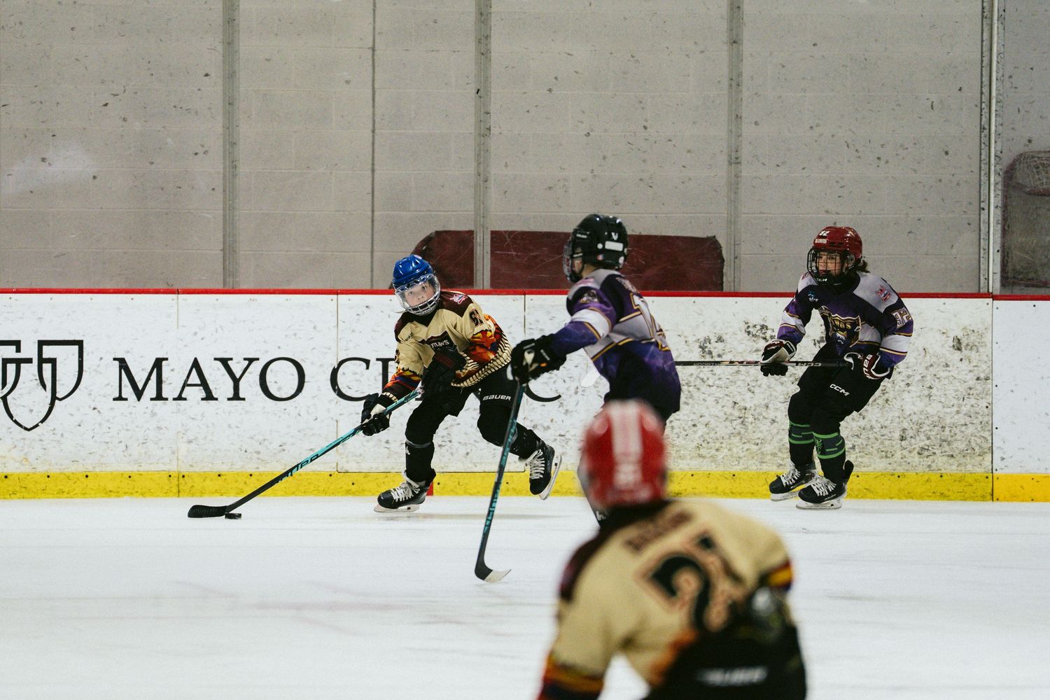 Three young youth hockey players compete for puck on ice during game at Mayo Clinic arena.