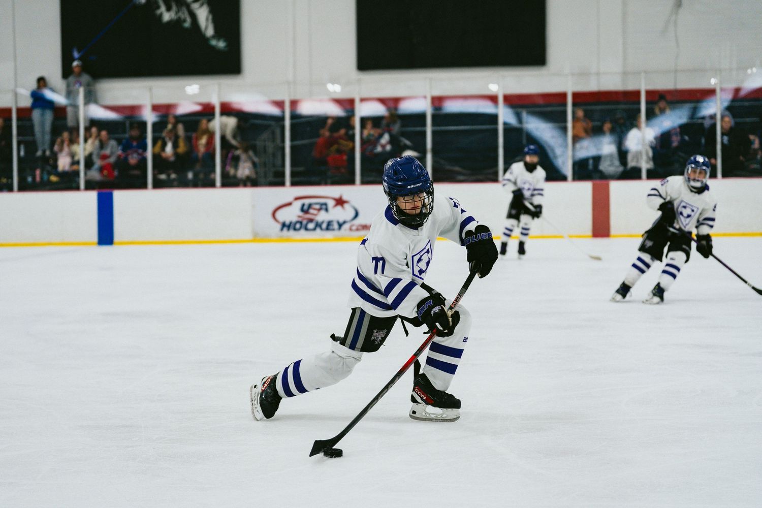Youth hockey player in white and blue uniform handles puck during game play.