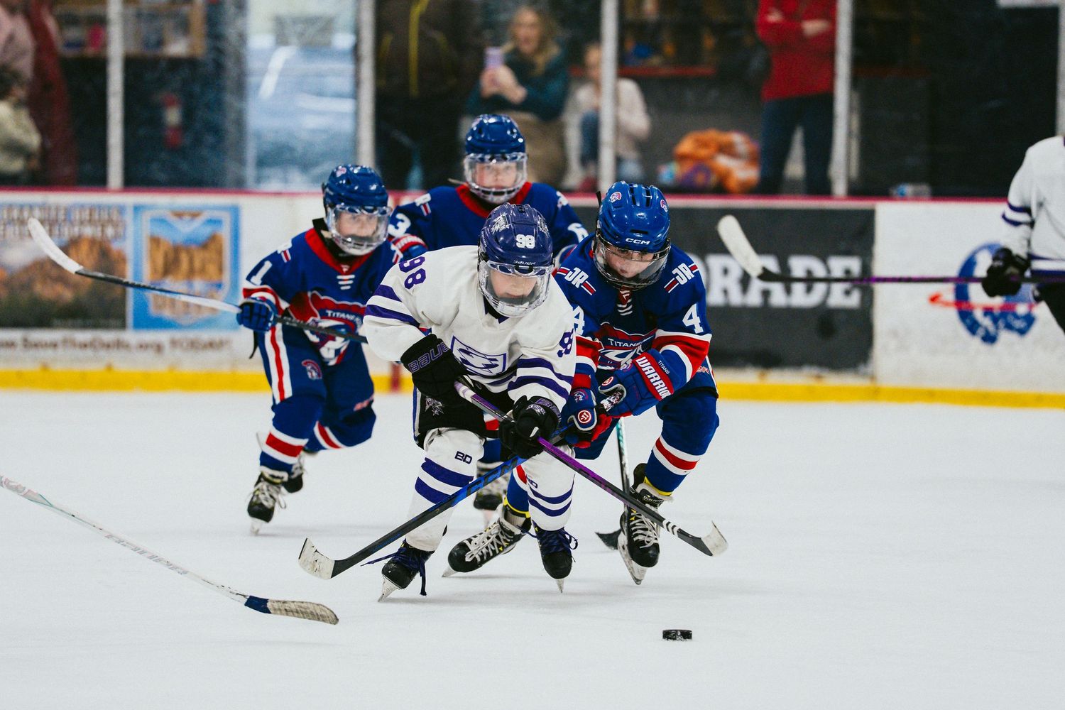 Youth hockey players battle for puck control during intense game action.