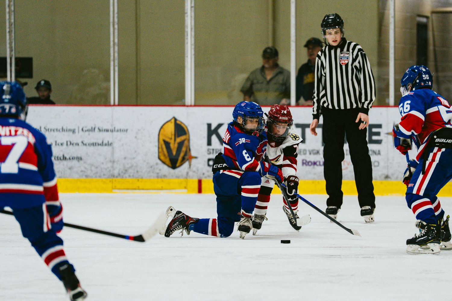 Hockey players scramble for the puck while a referee watches the play unfold.