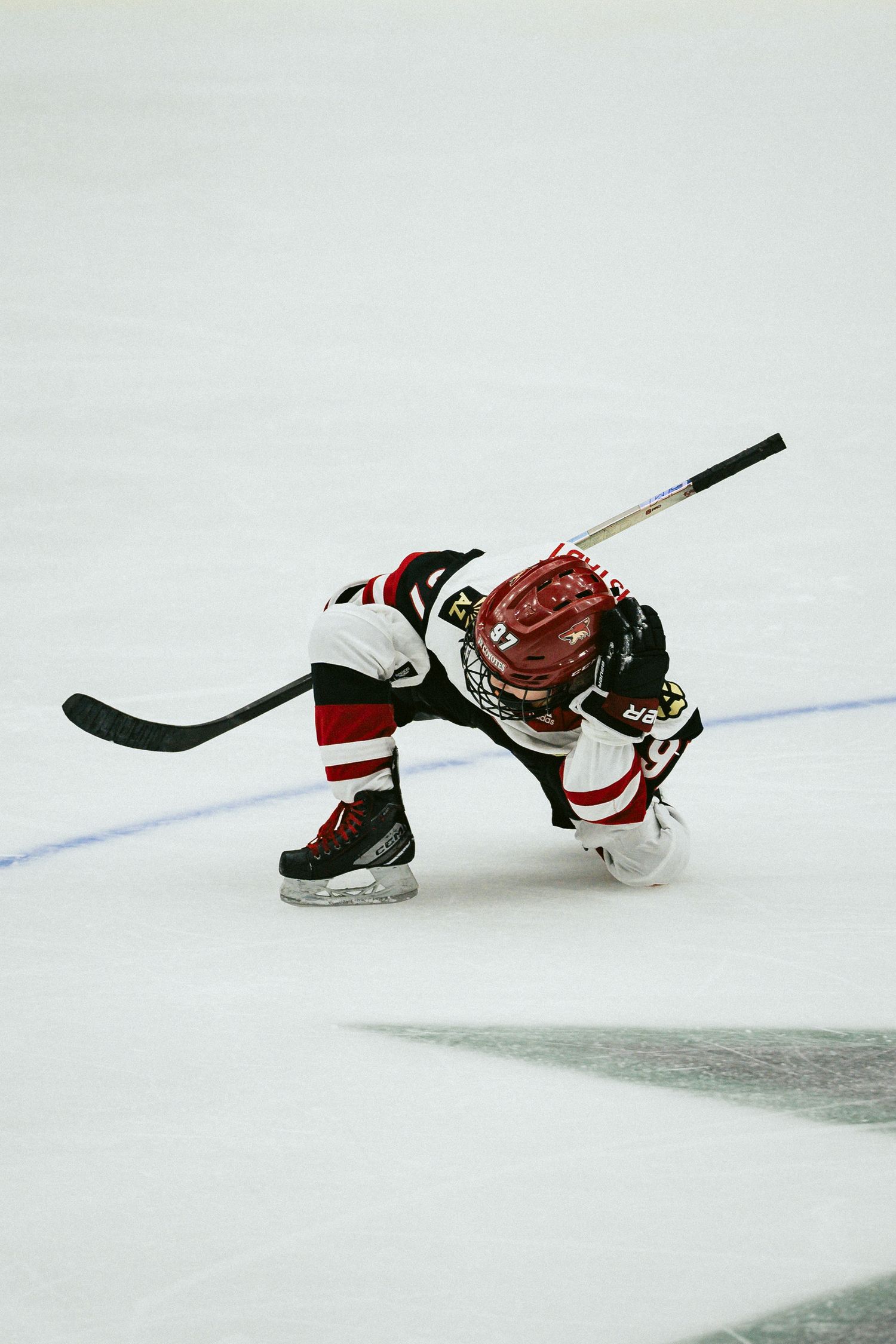Hockey player in red and white uniform makes dramatic diving motion on ice.