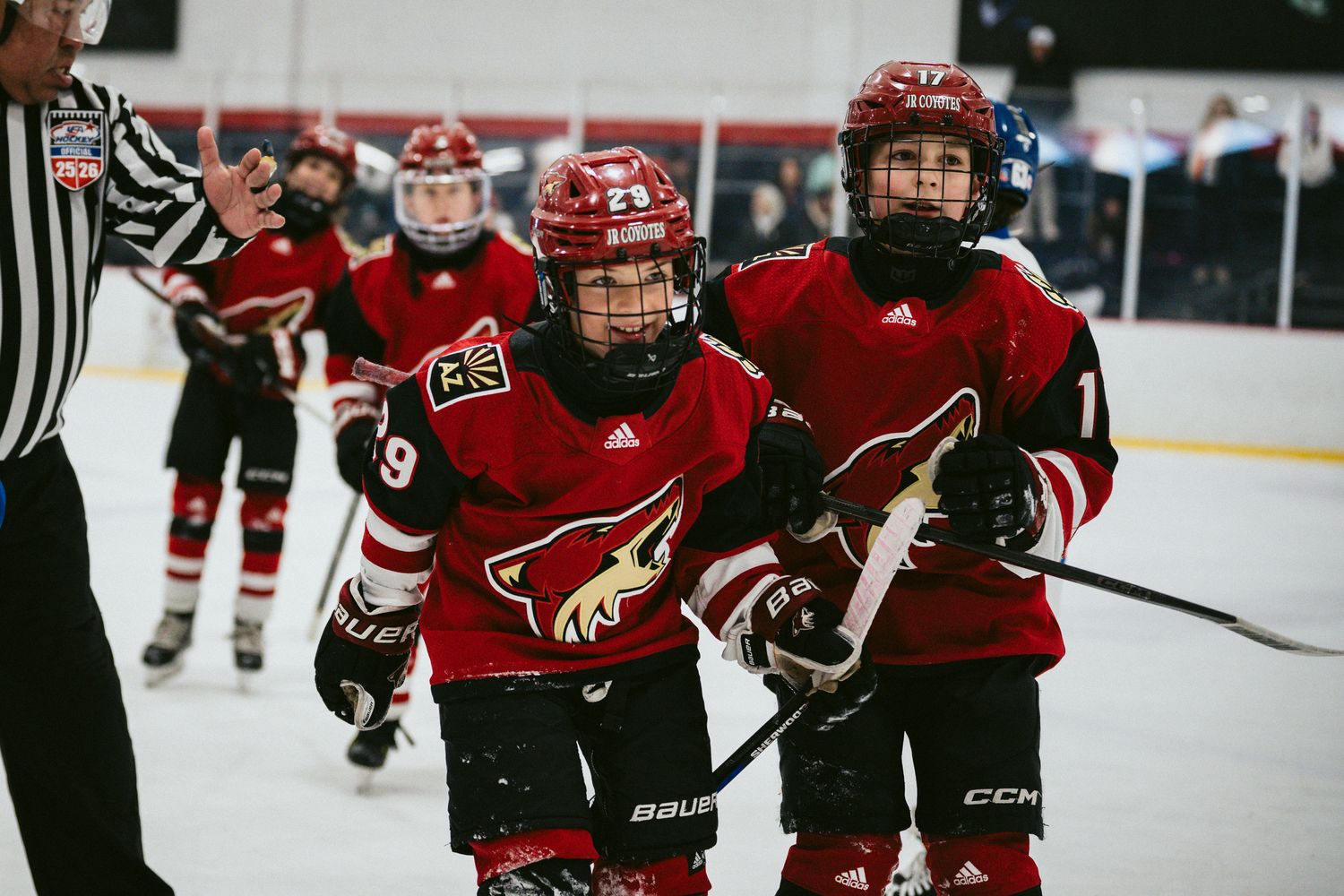 Youth hockey team in red and black uniforms skates on ice during gameplay.