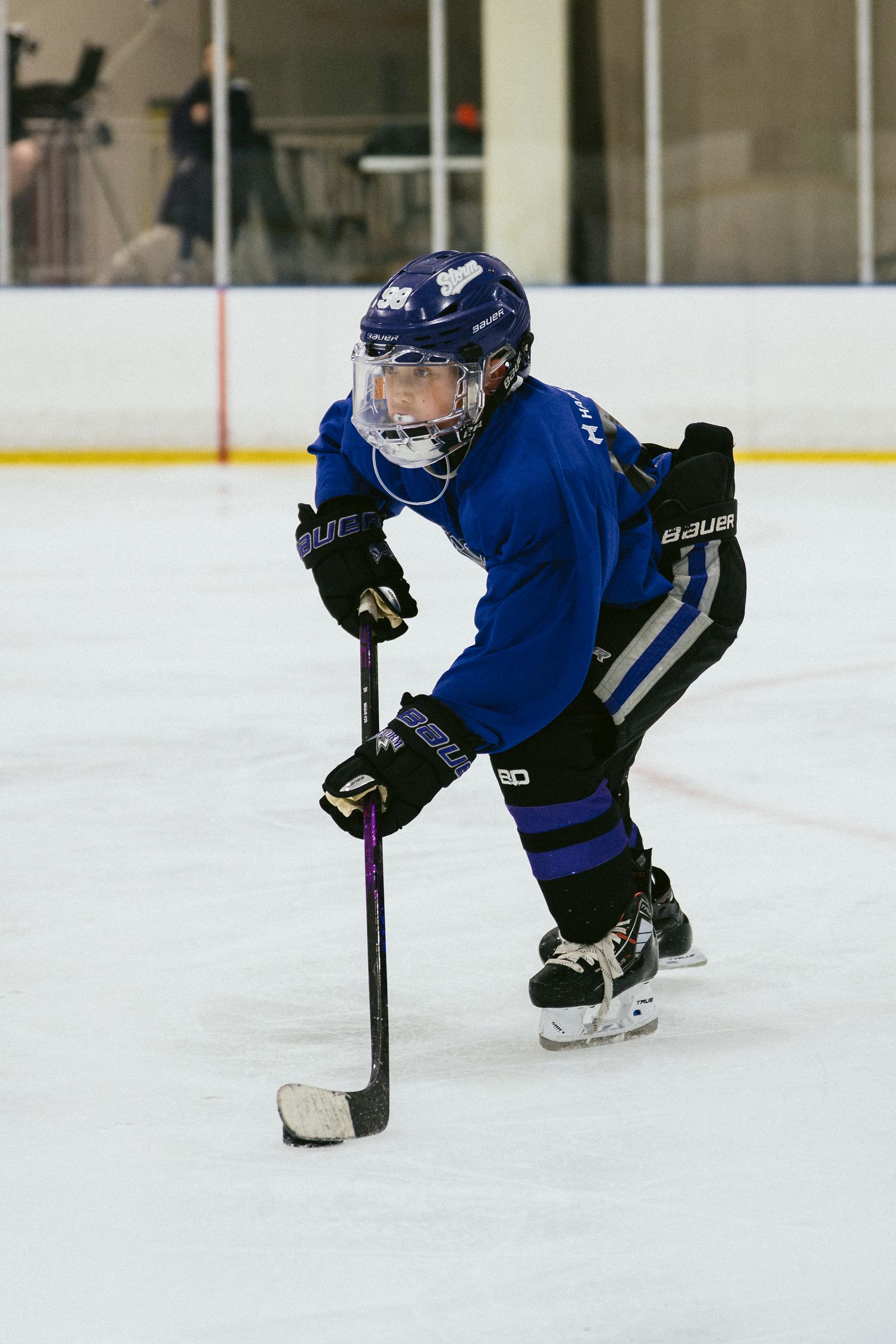 Young hockey player in blue uniform controls puck on ice rink during youth hockey game.