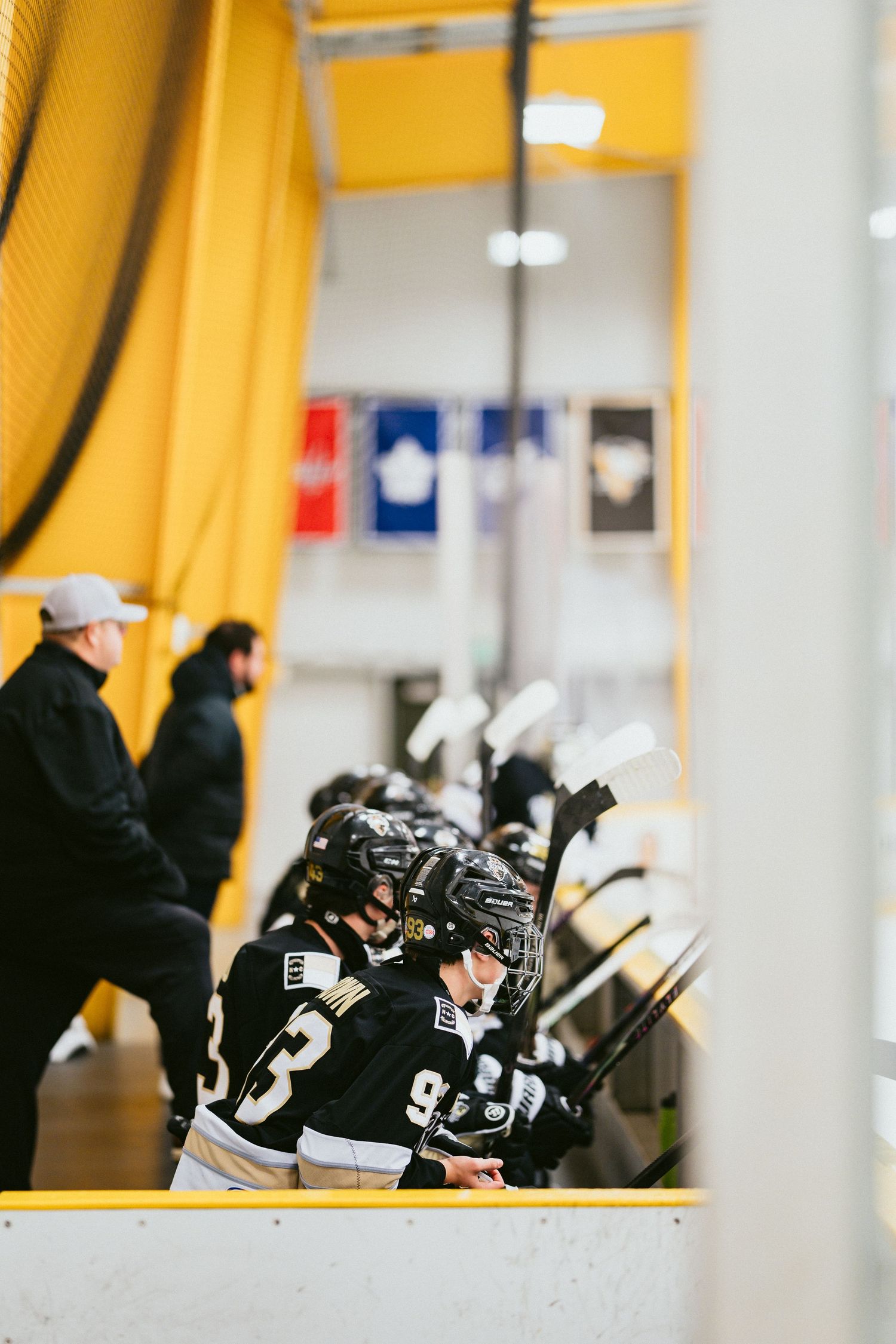 Youth hockey players in black jerseys wait in the tunnel before taking the ice at an indoor hockey arena.