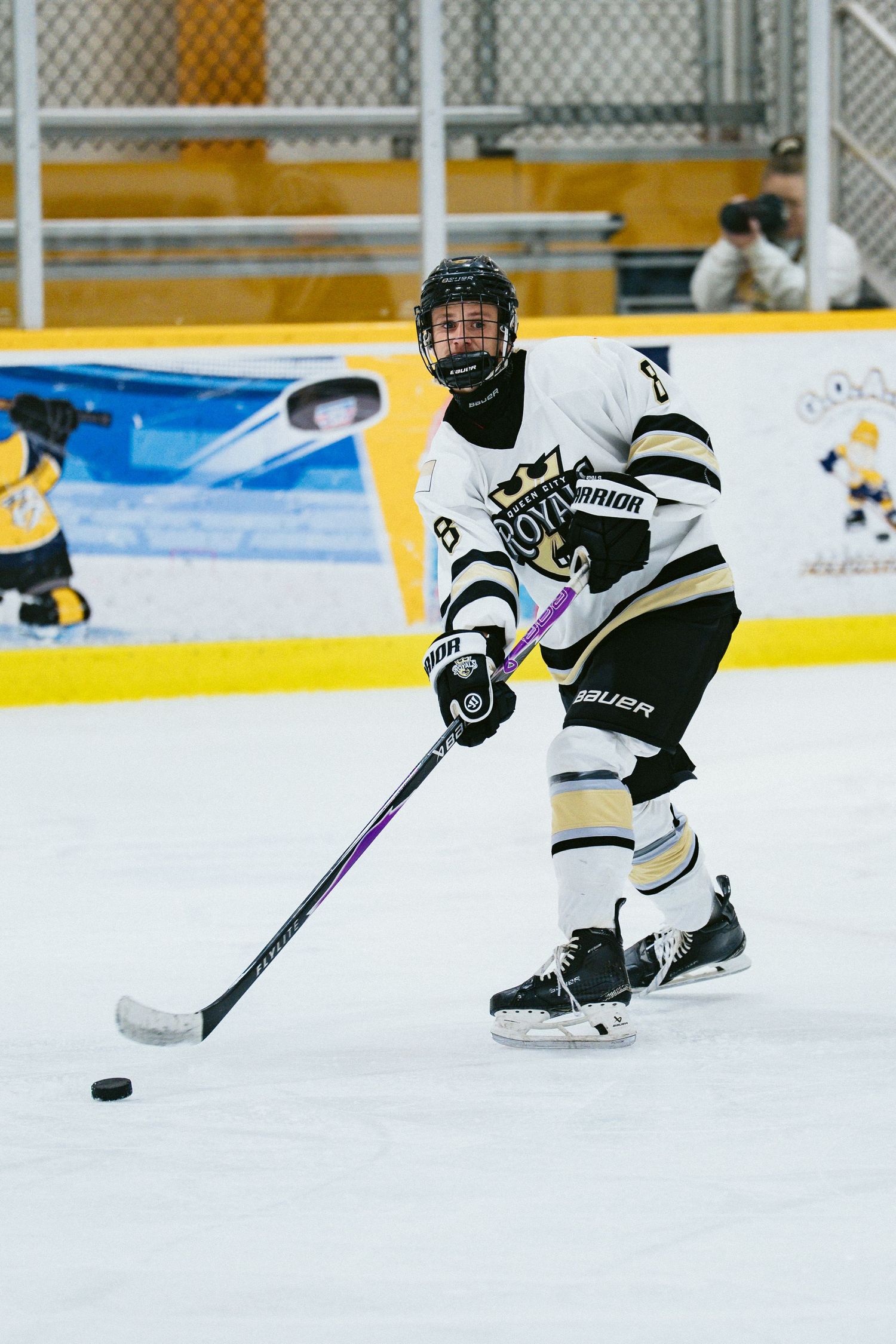 Hockey player in black and white crown jersey skates with the puck during an indoor game.