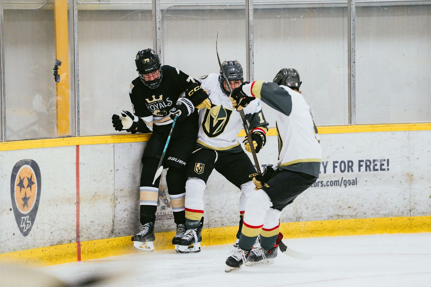 Hockey players battle along the boards during an intense ice hockey game at an indoor rink.