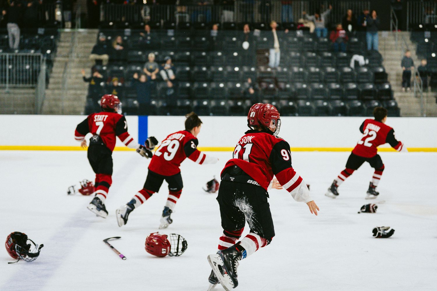 Hockey players in red uniforms celebrating victory by throwing equipment on ice.