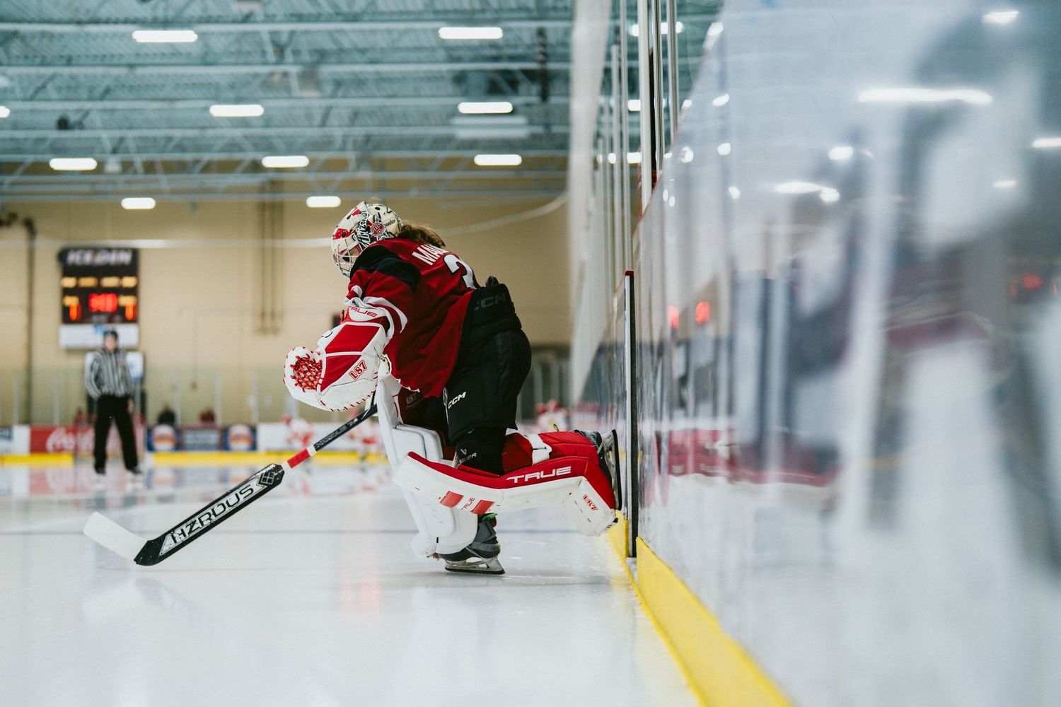 Hockey player in red jersey performs dynamic skating maneuver along the boards during indoor game.