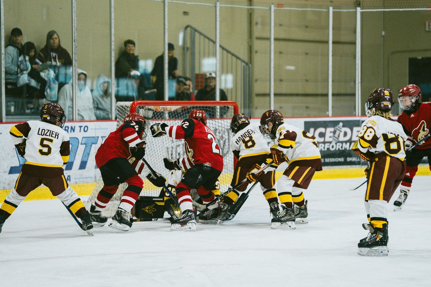 Hockey players scramble for the puck during an intense goal-mouth action between red and yellow teams.