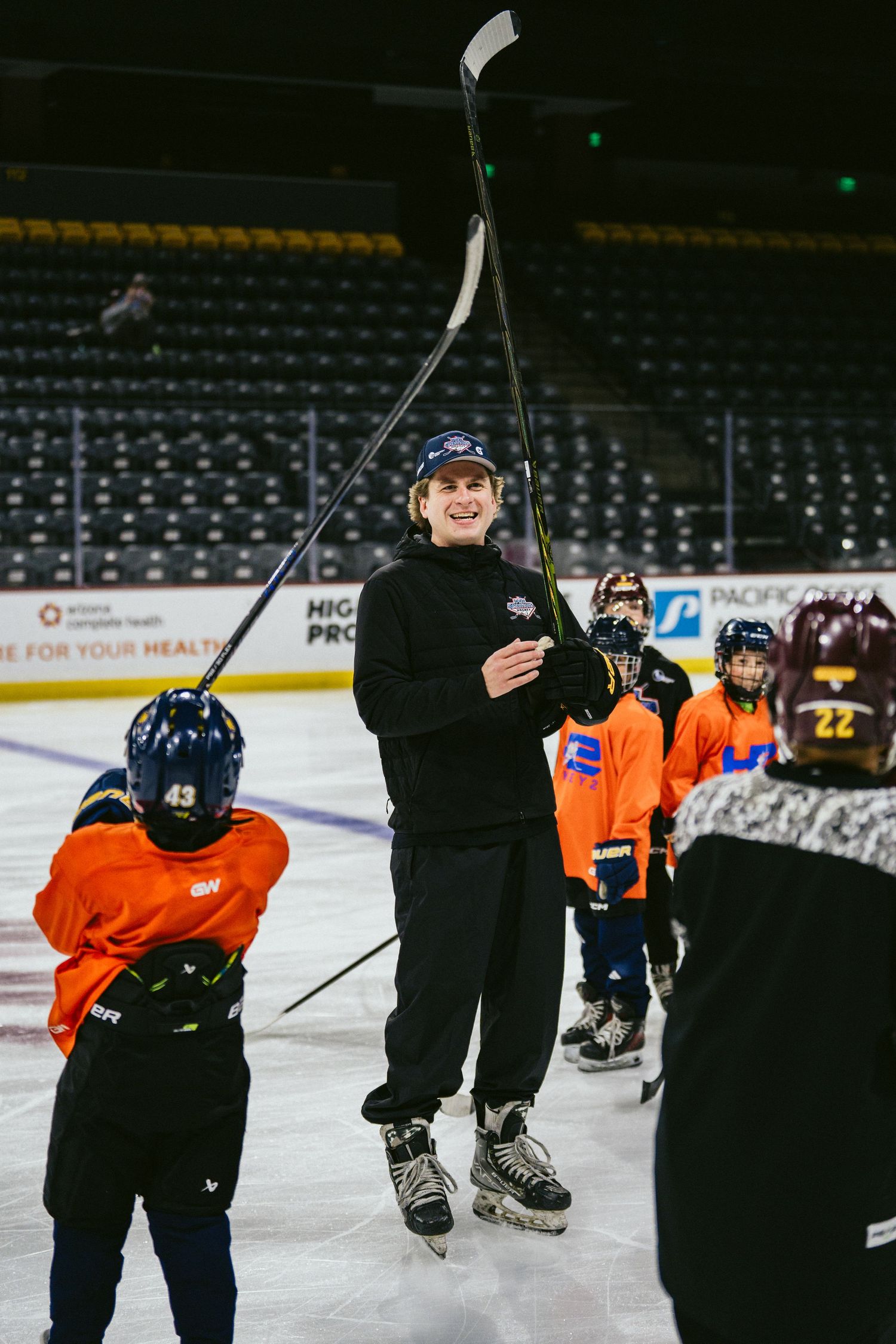 Hockey coach demonstrating stick technique to young players during an ice hockey clinic.