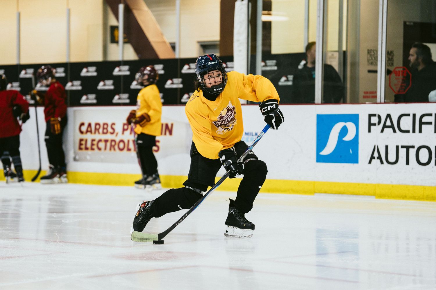 Youth hockey player in yellow jersey skating with stick during ice hockey practice at indoor arena.