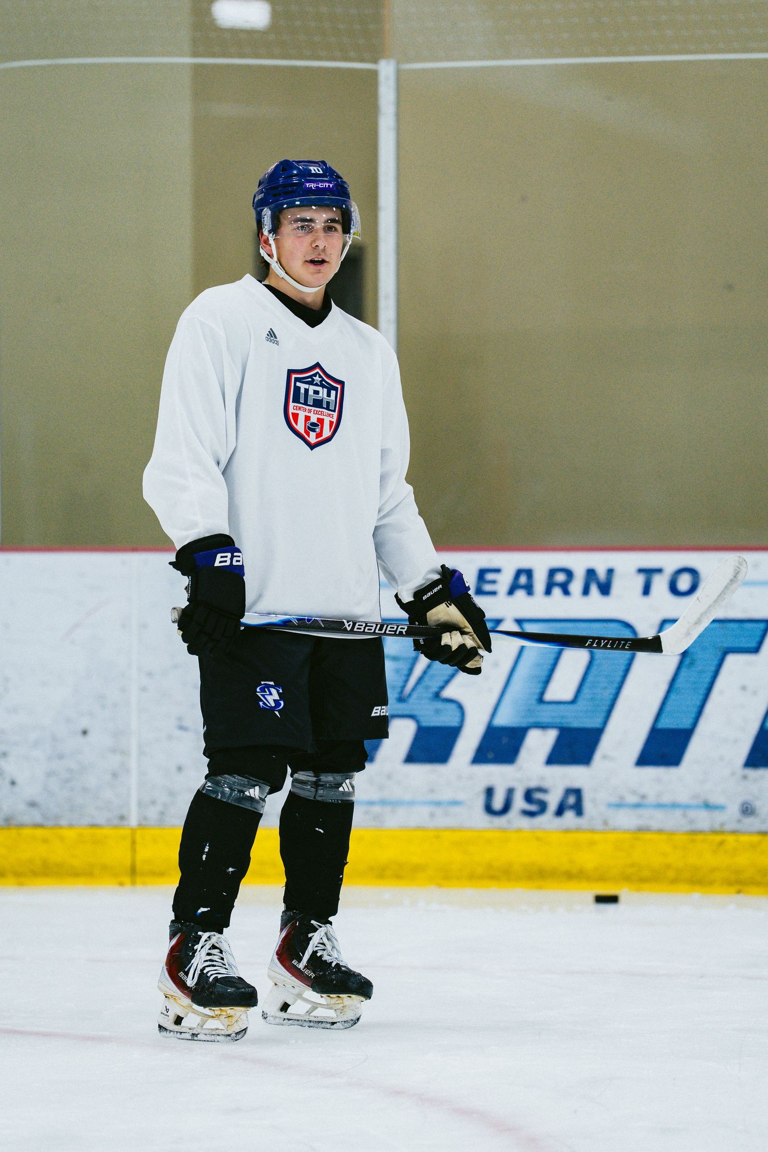 Young male hockey player in white TPLU jersey stands on ice during training session.