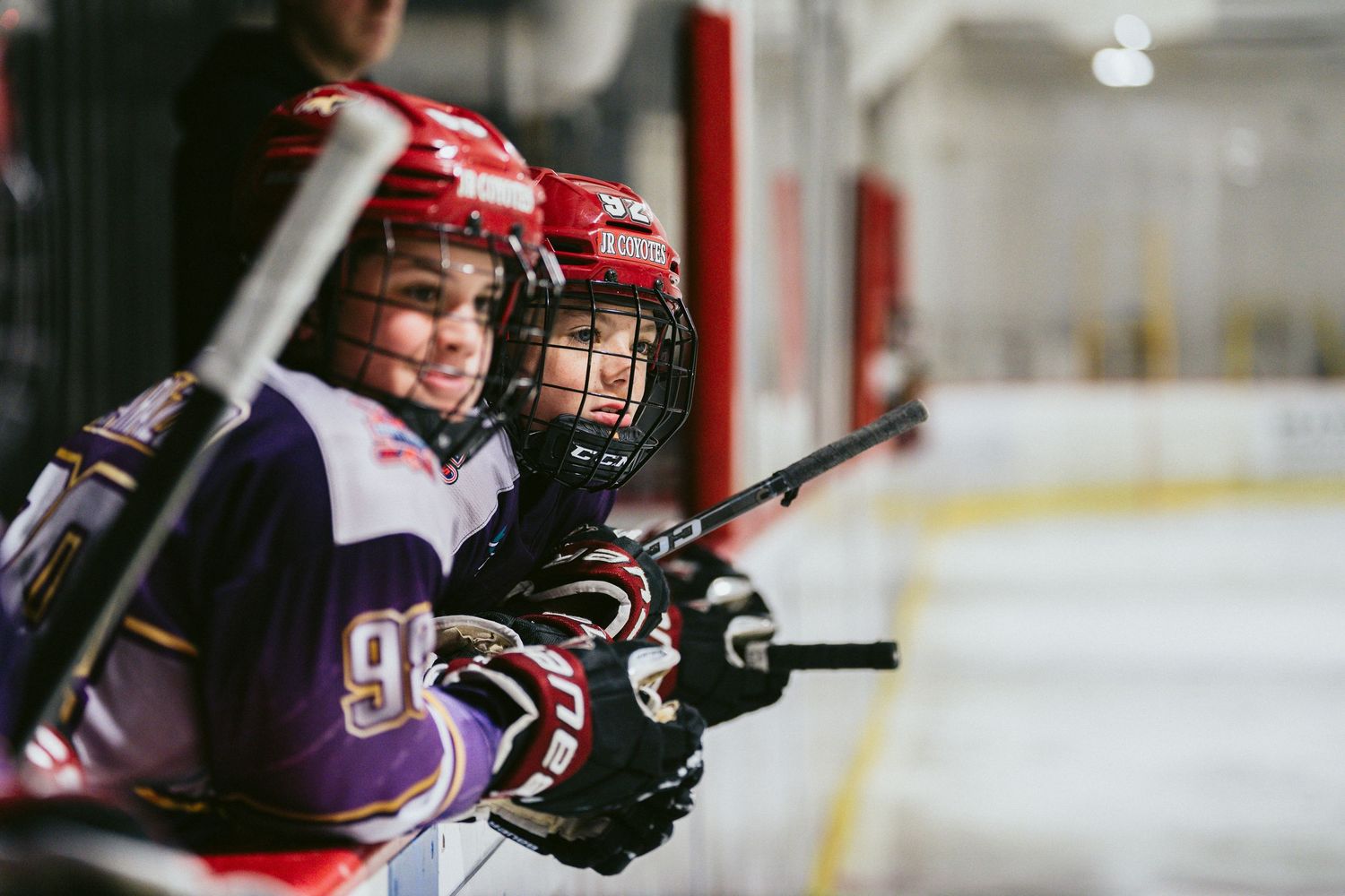Young ice hockey players smile on the bench during a youth hockey tournament game.