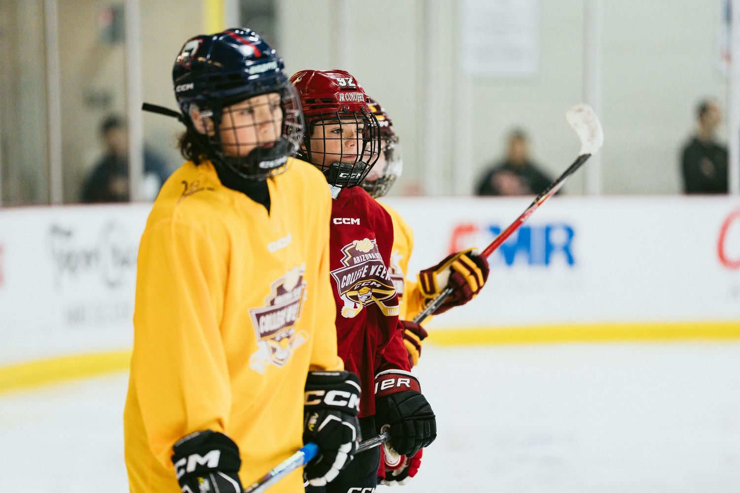 Two young hockey players in yellow and red jerseys stand on the ice during a youth hockey camp.