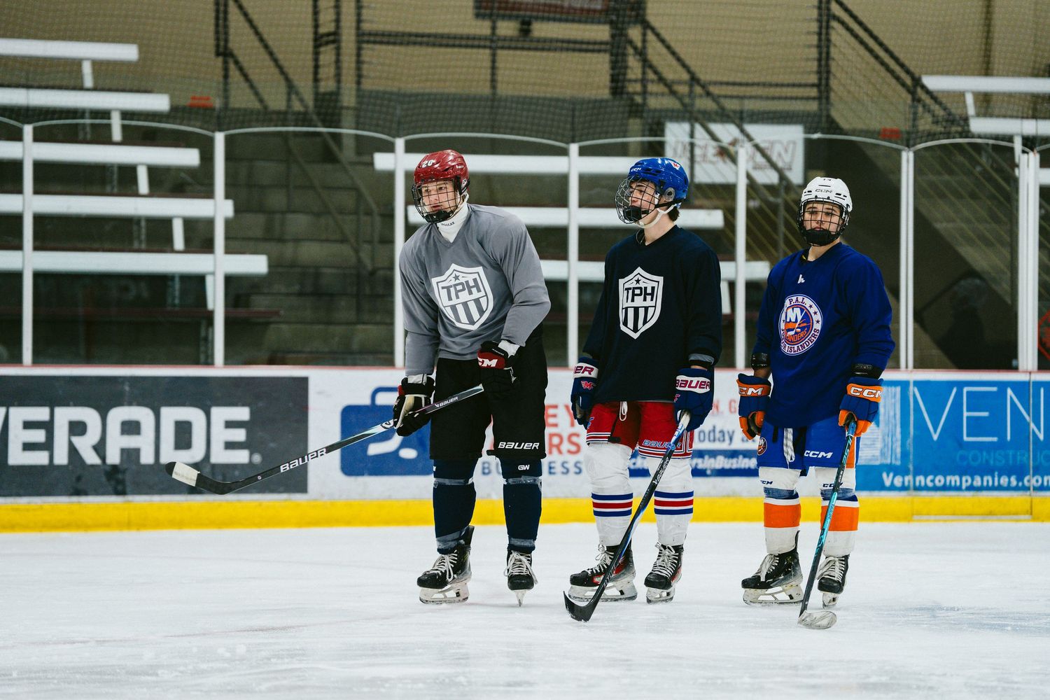 Three youth hockey players stand on ice rink during team practice session wearing helmets and jerseys.