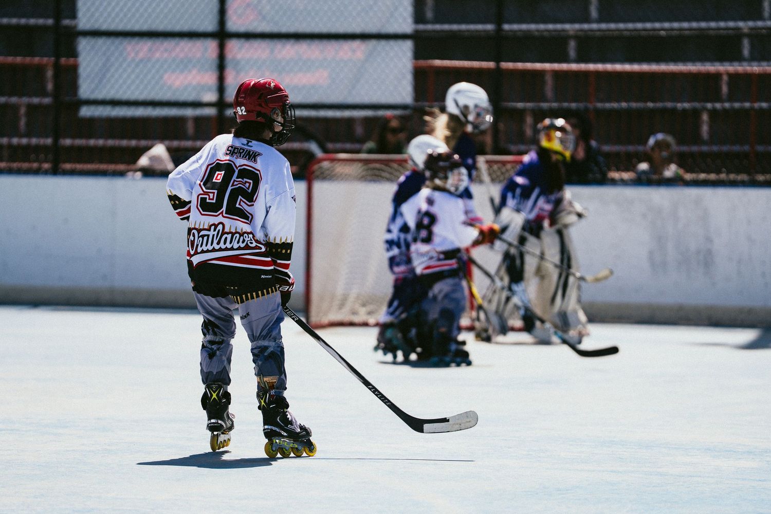 Youth roller hockey player wearing number 92 Outlaws jersey stands near goal during outdoor rink game.