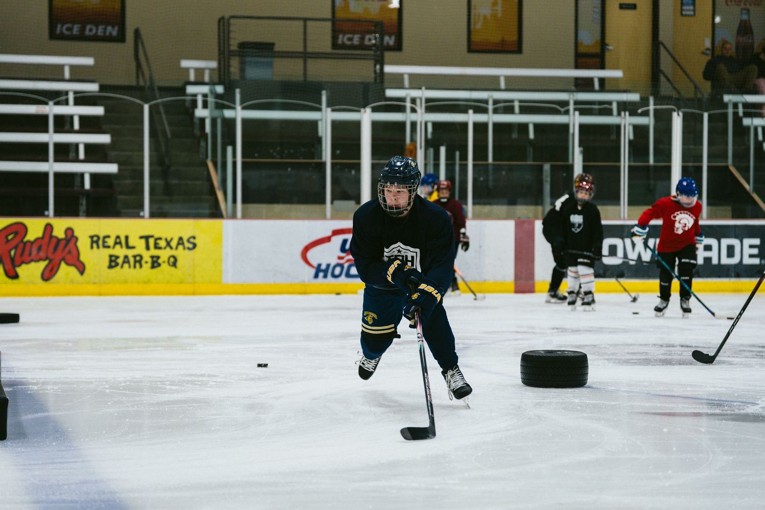 Young hockey player in navy uniform handles the puck during an indoor ice hockey practice drill.