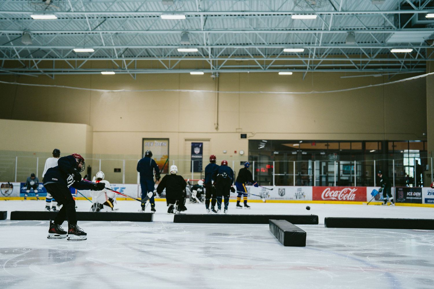 Hockey players practice drills on an indoor ice rink with Coca-Cola advertising boards visible in the background.
