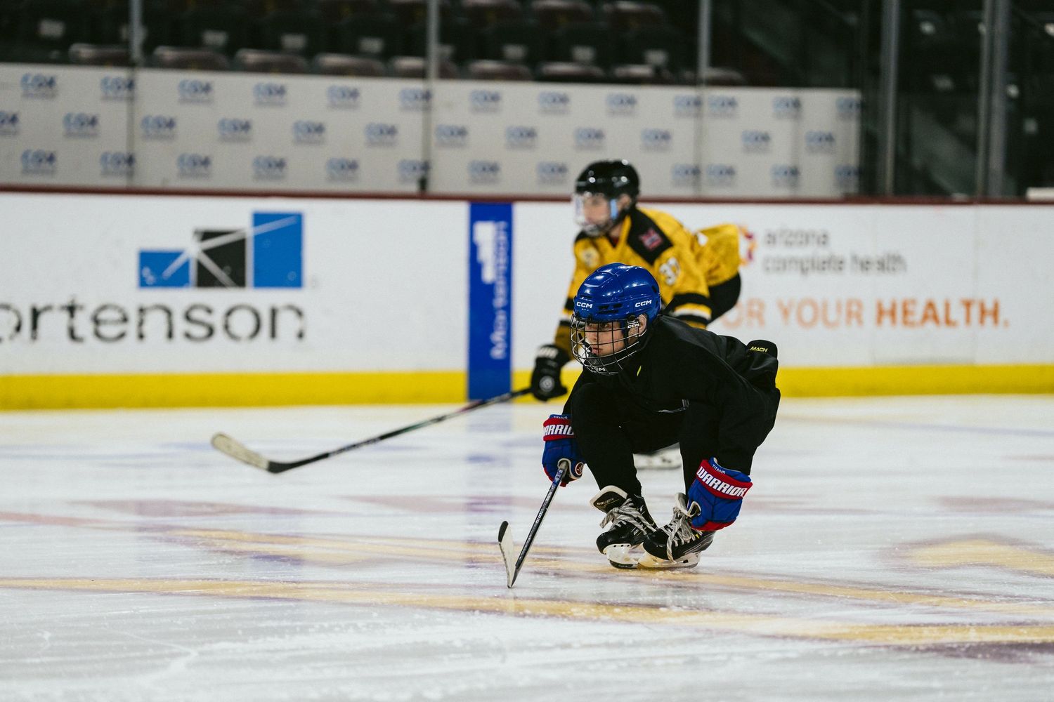 Youth ice hockey players compete on an indoor rink during a game, wearing full protective gear.