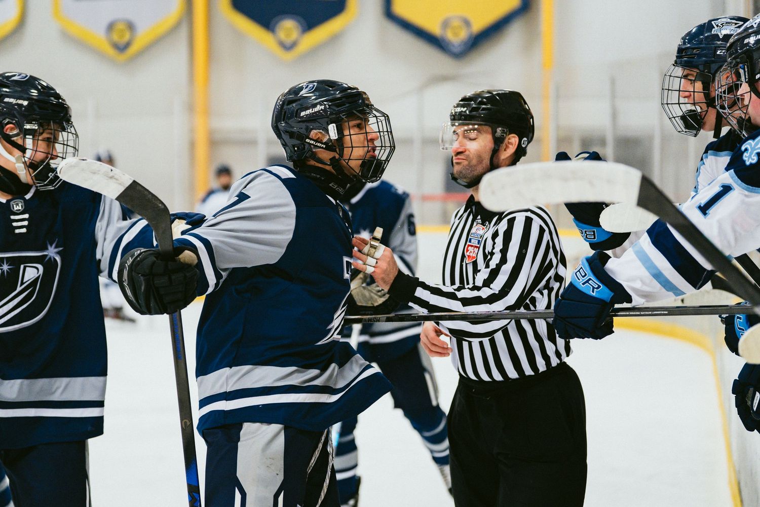 Hockey referee separating two players during a tense moment on the ice rink during a competitive game.