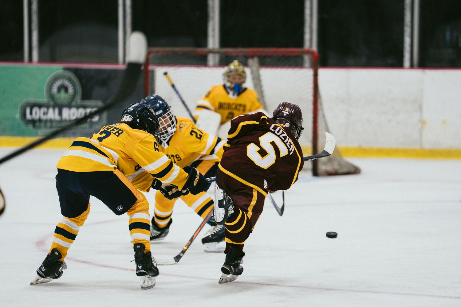 Two ice hockey players battle for the puck during a competitive game, with a goalie guarding the net in the background.