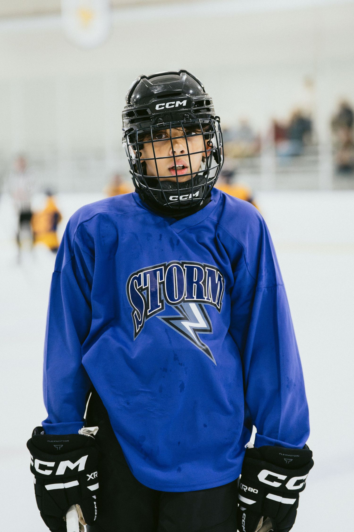 Young hockey player in blue Storm jersey and CCM helmet standing on ice rink during practice.