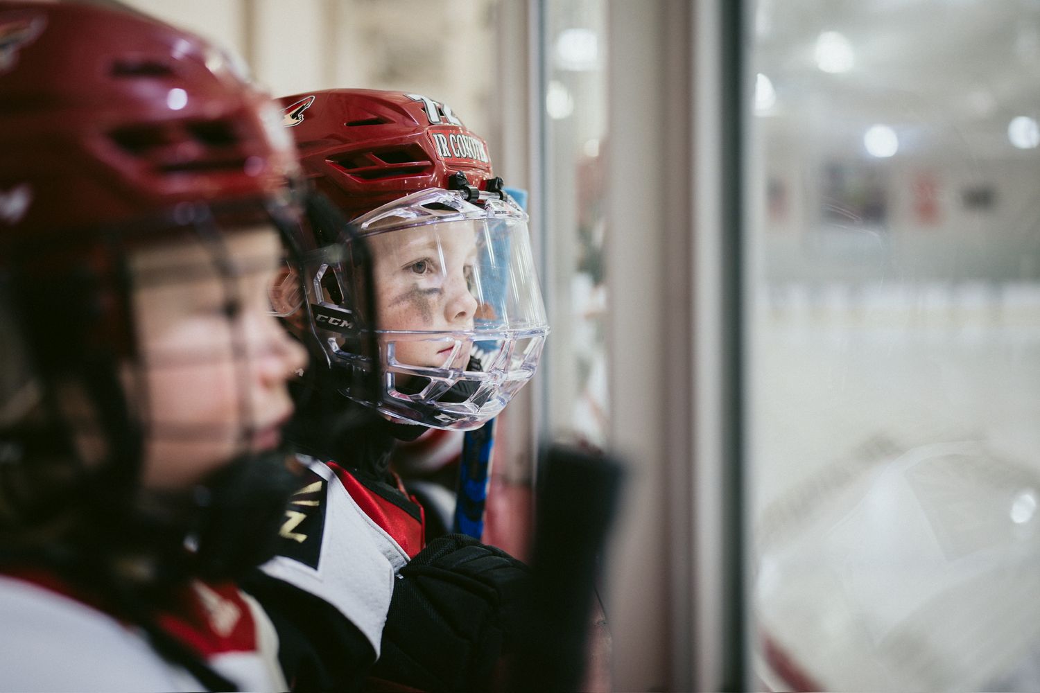 Hockey players watching game through glass barrier at ice rink.