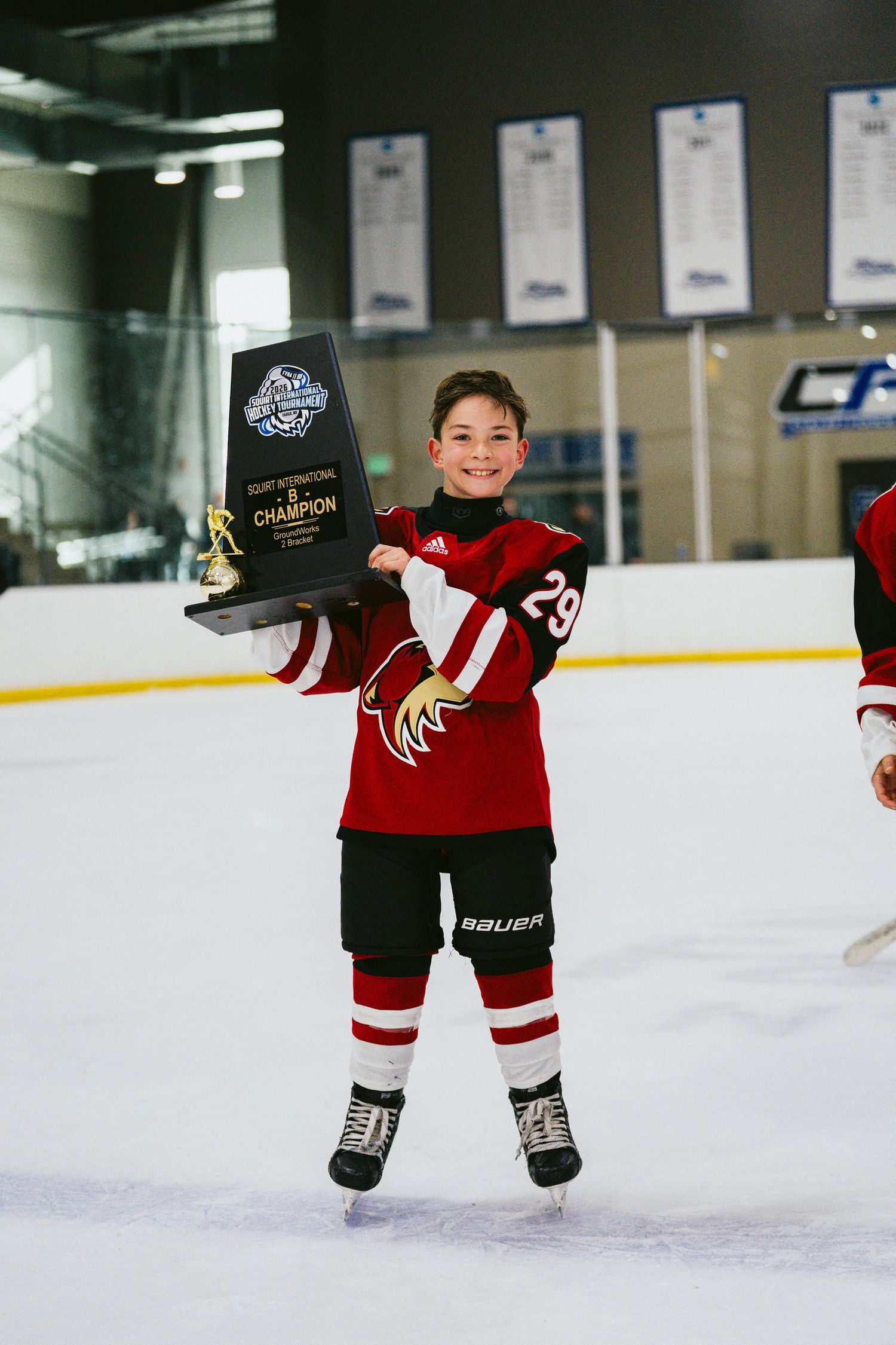 Young athlete in red hockey uniform shows off championship award while skating.