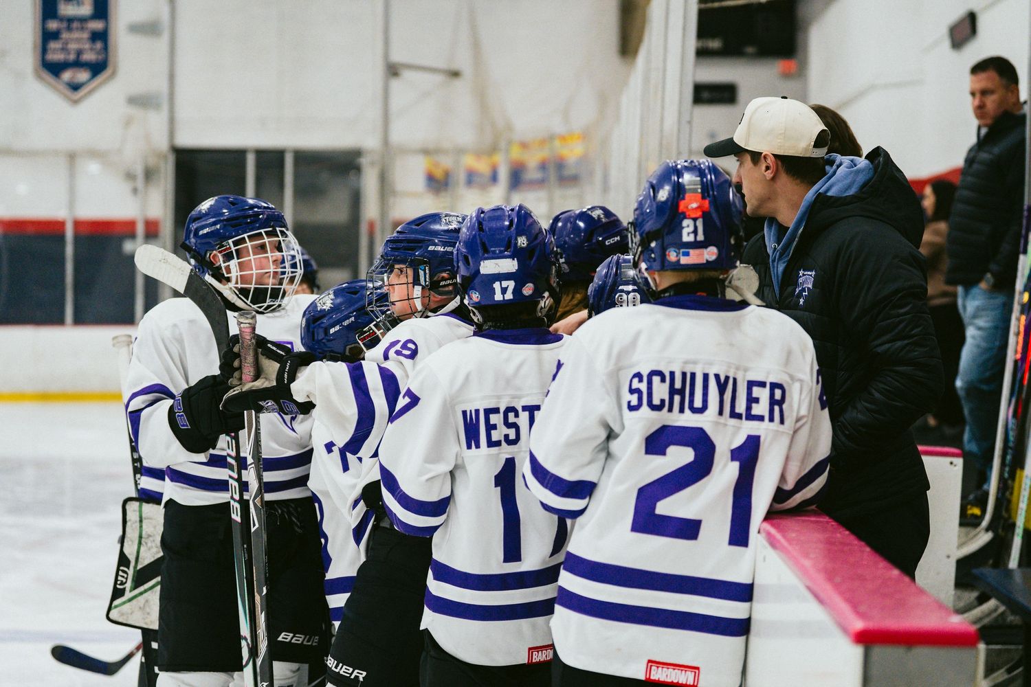 Hockey players in blue and white uniforms line up along the boards during practice.