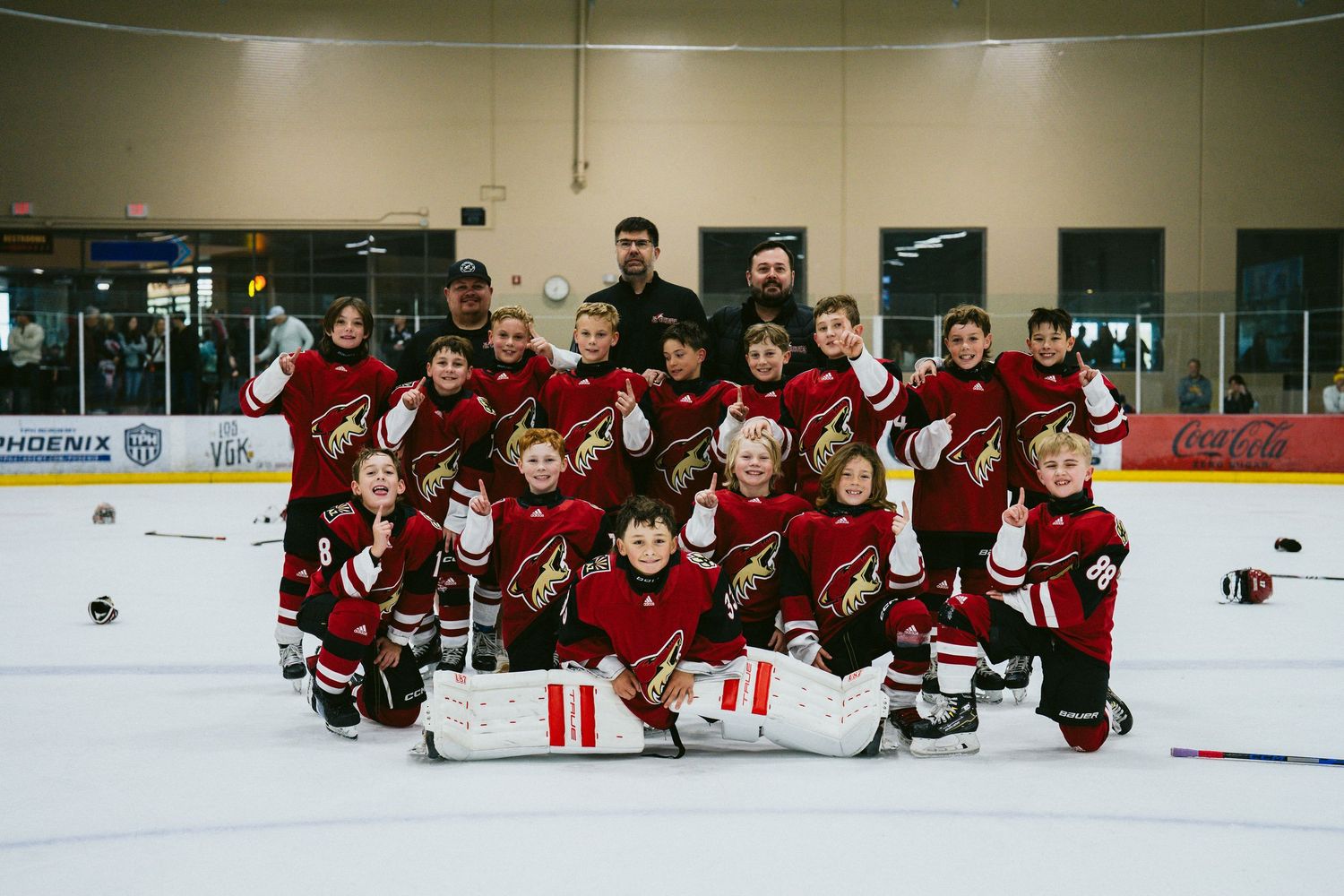 Youth hockey team poses for traditional team photo on the ice in red uniforms.