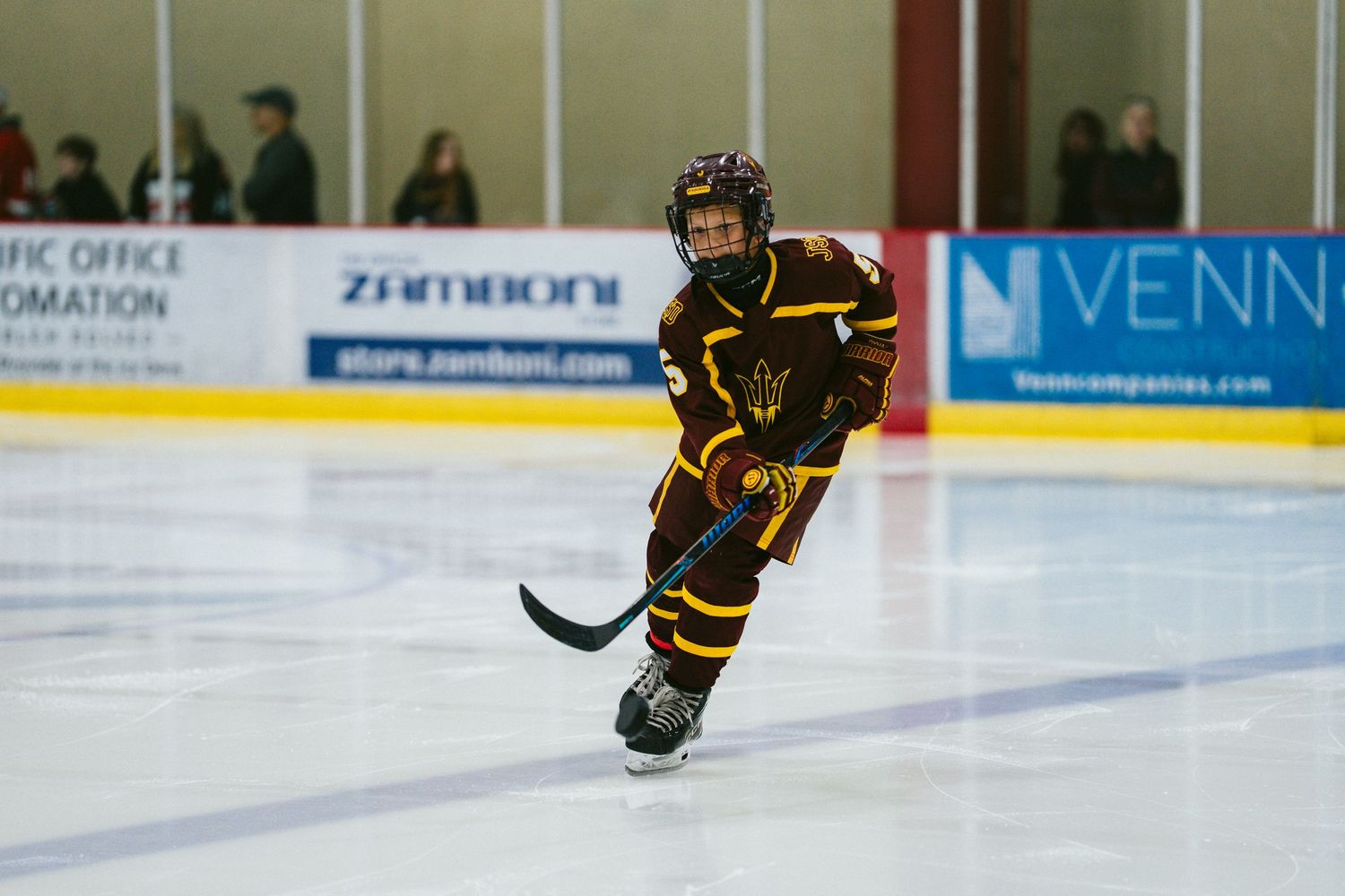 Youth hockey player in black and gold jersey skating on ice during a match.
