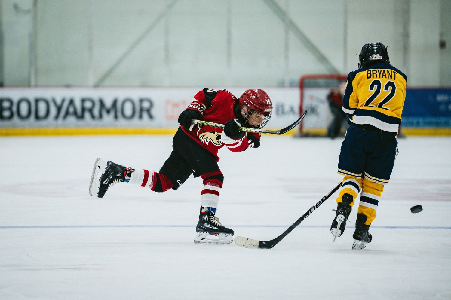 Hockey players in red and yellow jerseys chase after the puck during a game.