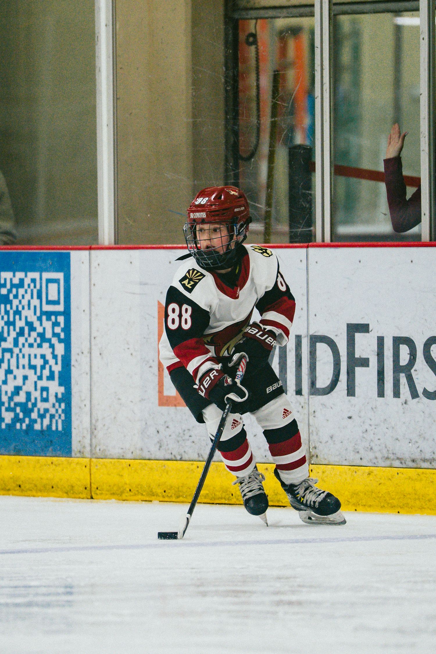 Young hockey player in dark jersey handles puck near the boards during game action.