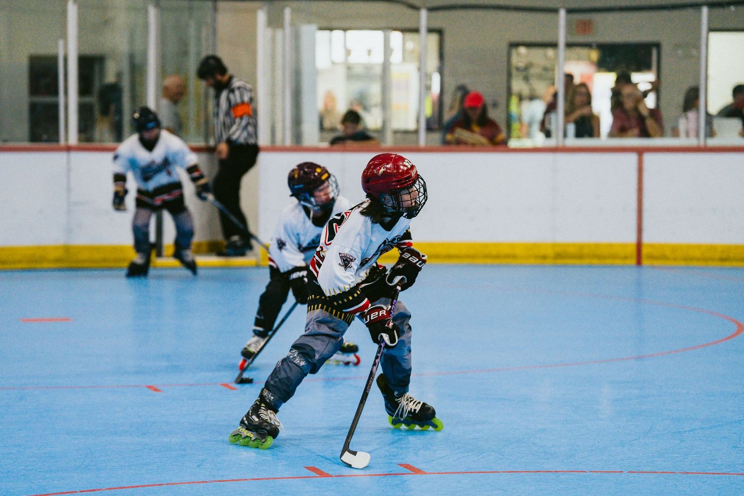 Two young children play roller hockey on an indoor rink wearing full protective gear.