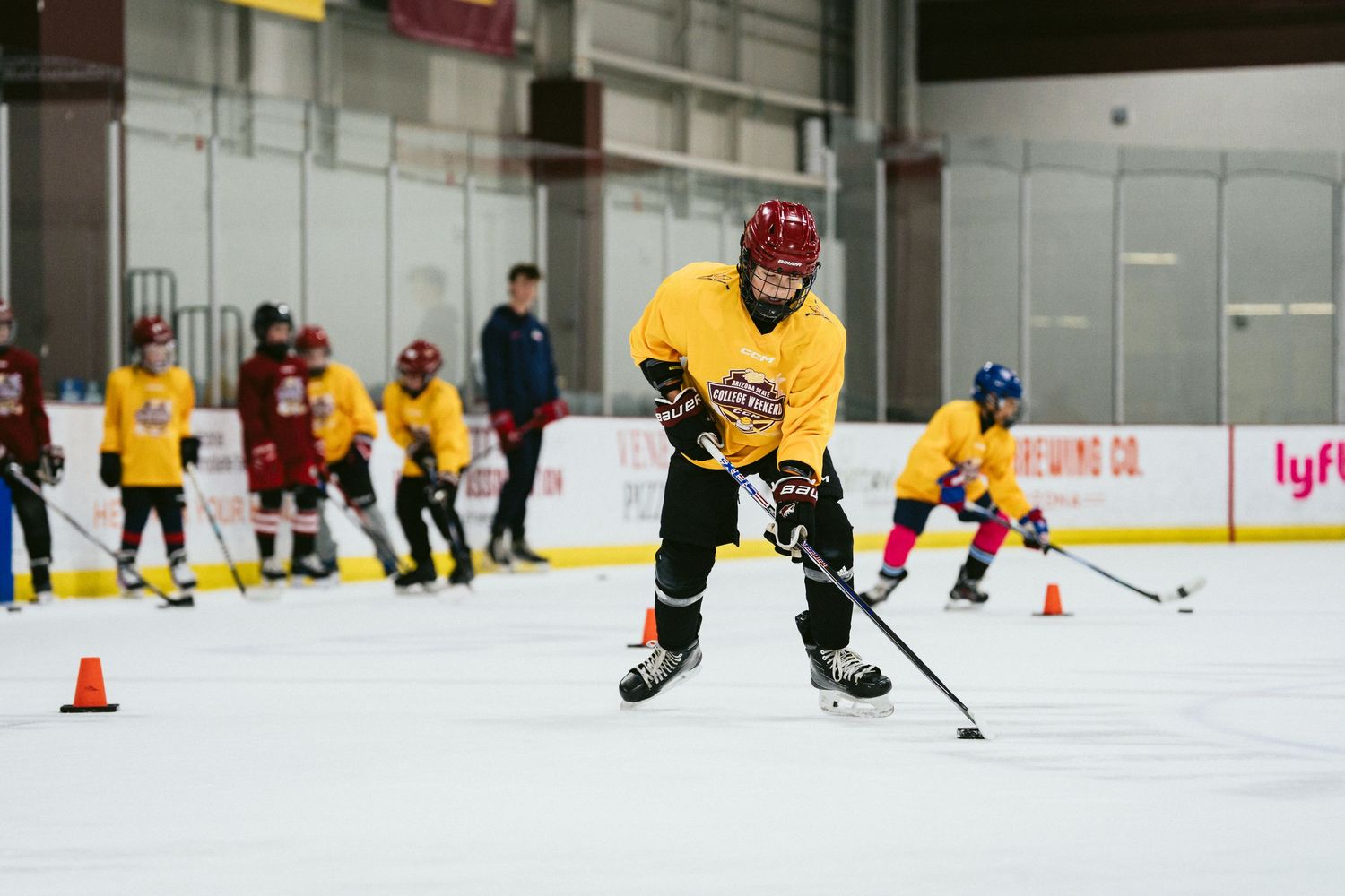 Young hockey player in yellow jersey practices puck handling drills on indoor ice rink during training session.