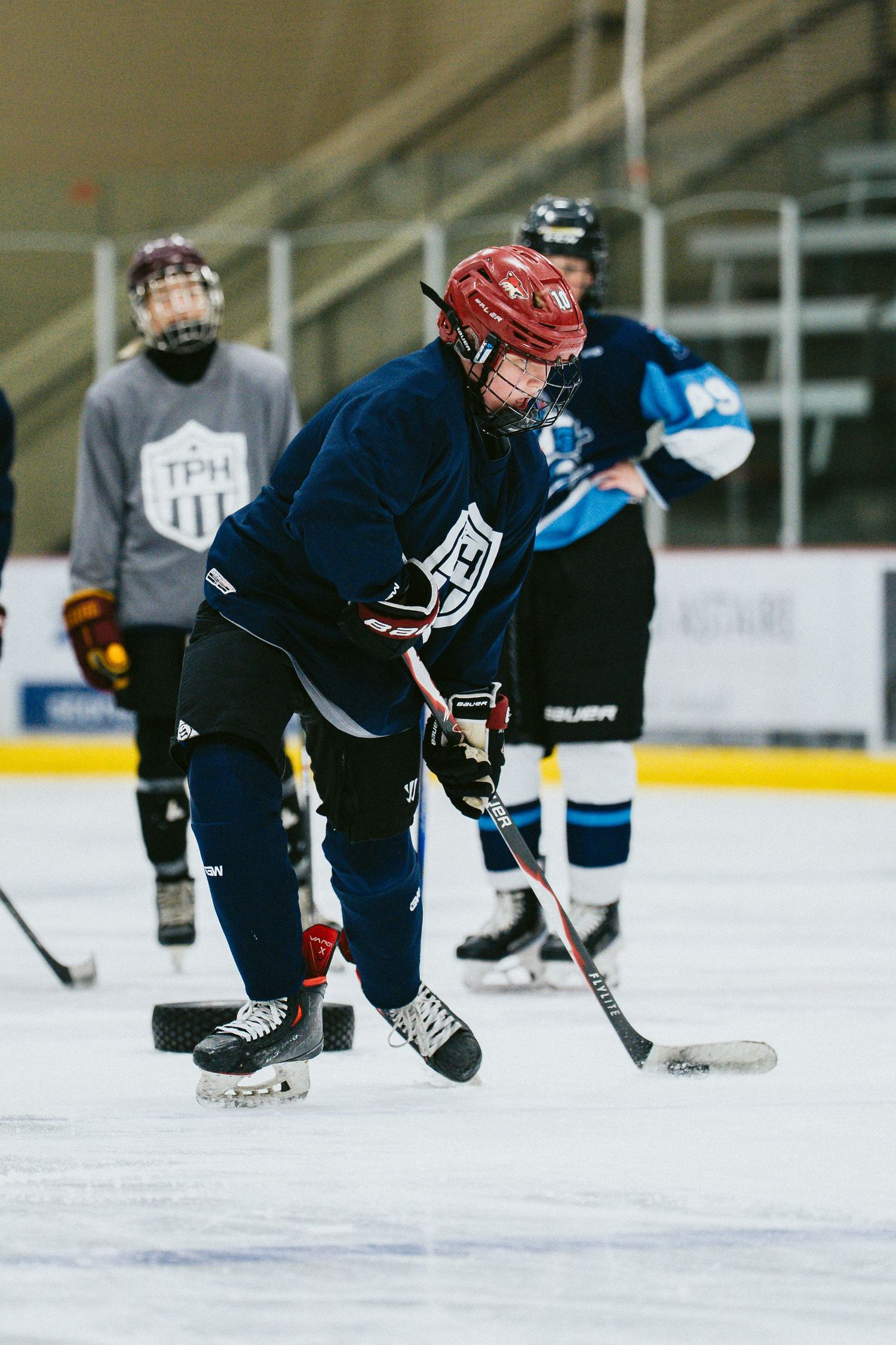 Young hockey player in red helmet and blue jersey handles puck on ice during practice drill at indoor rink.