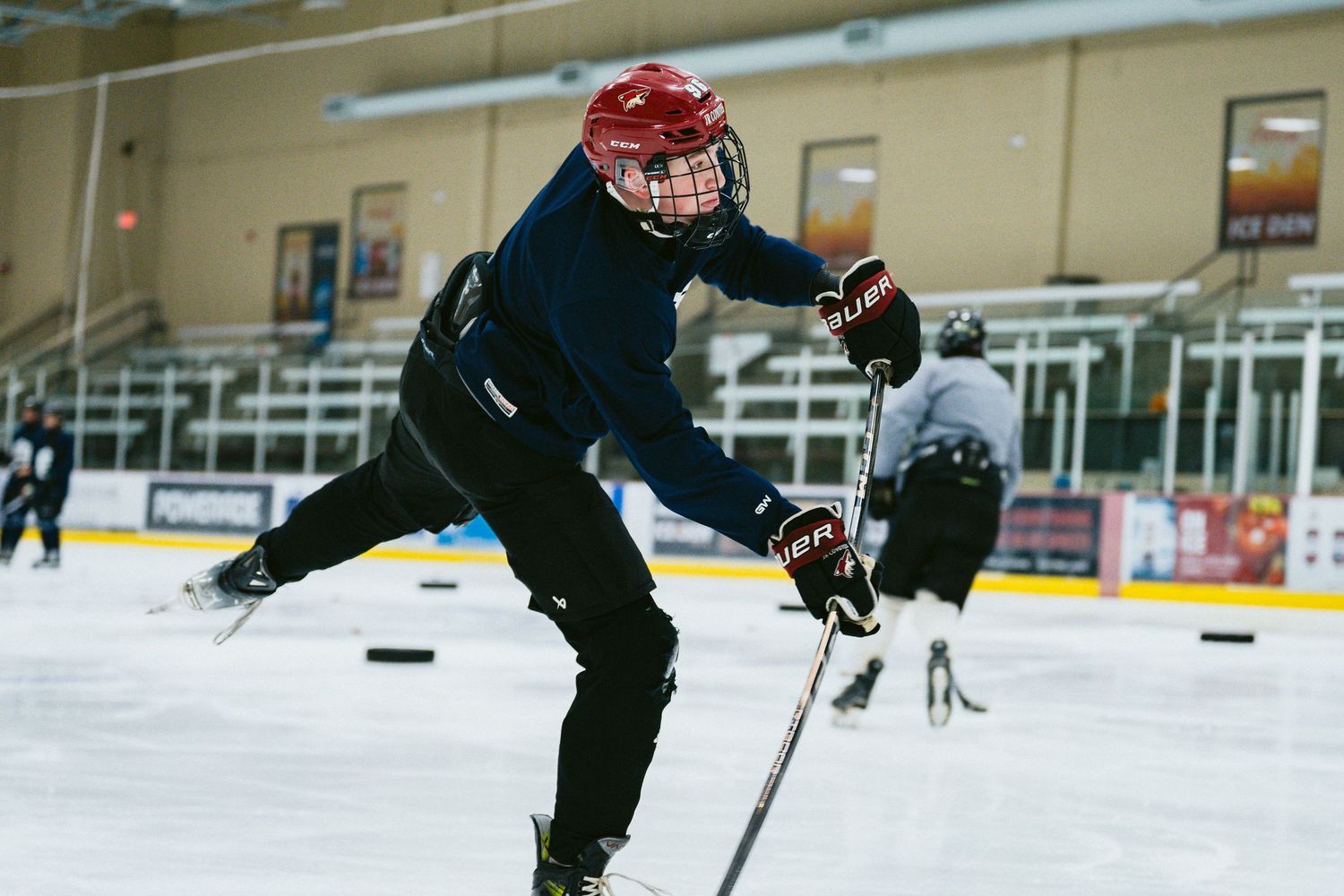 Youth hockey player in red helmet takes a powerful shot on the ice during TPH hockey practice.