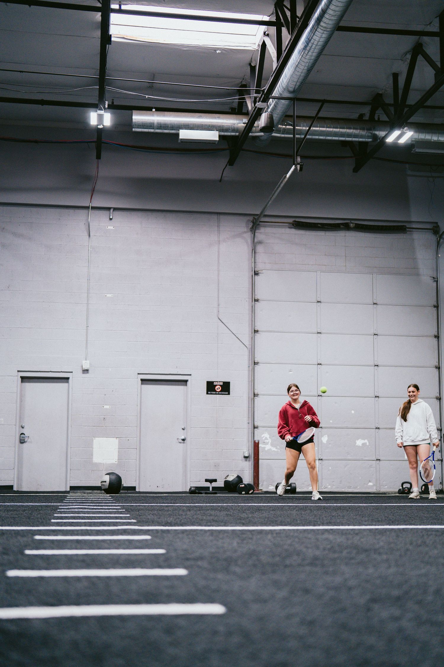 Two women training on an indoor turf field at Ice Den Performance sports facility.